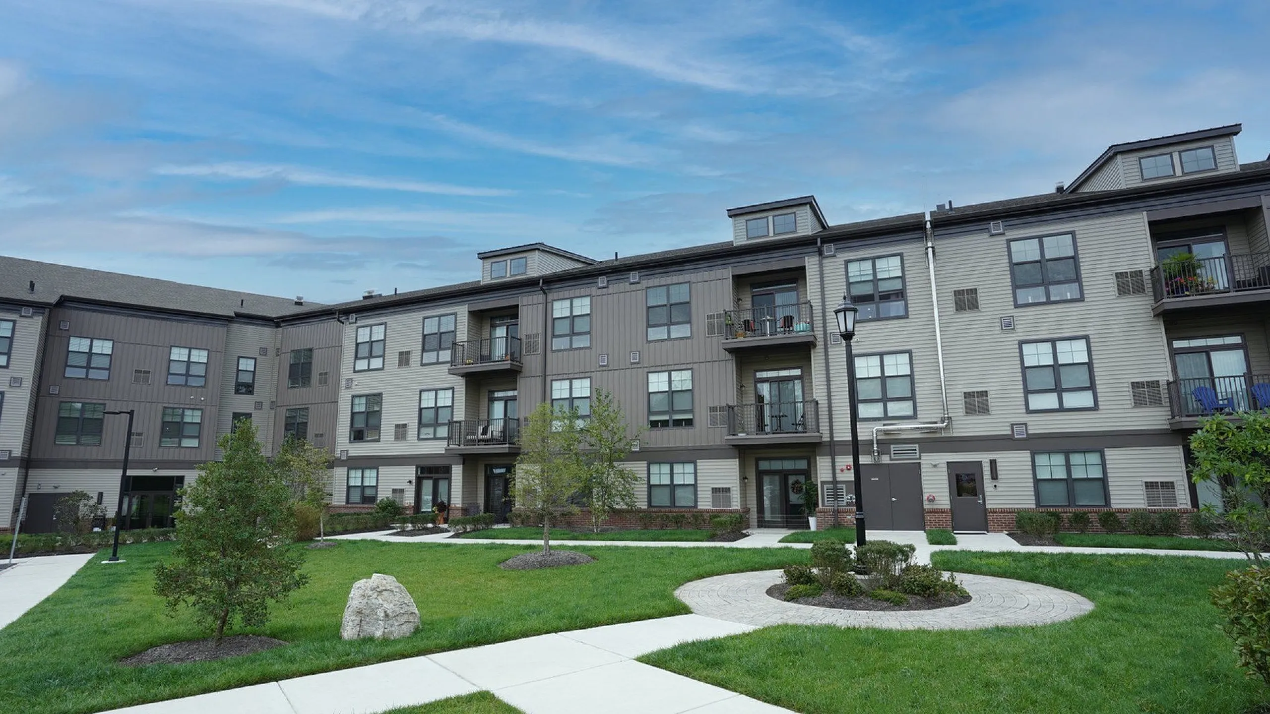 Modern apartment complex with elegant fa&ccedil;ade and manicured green lawns under a clear blue sky.