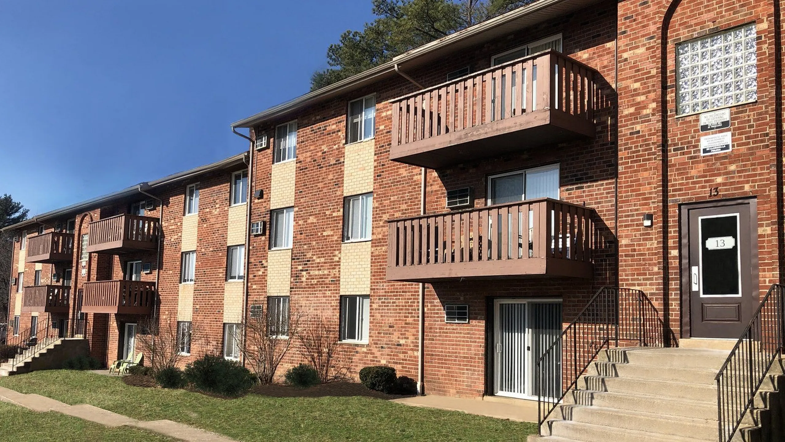 Charming brick apartment building with private balconies and lush green surroundings.
