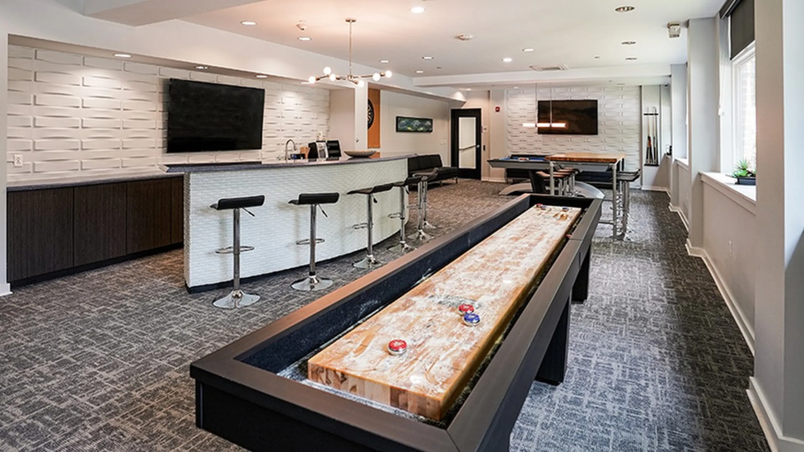 Chic apartment lounge featuring a sleek bar area, modern seating, and an entertaining shuffleboard setup.