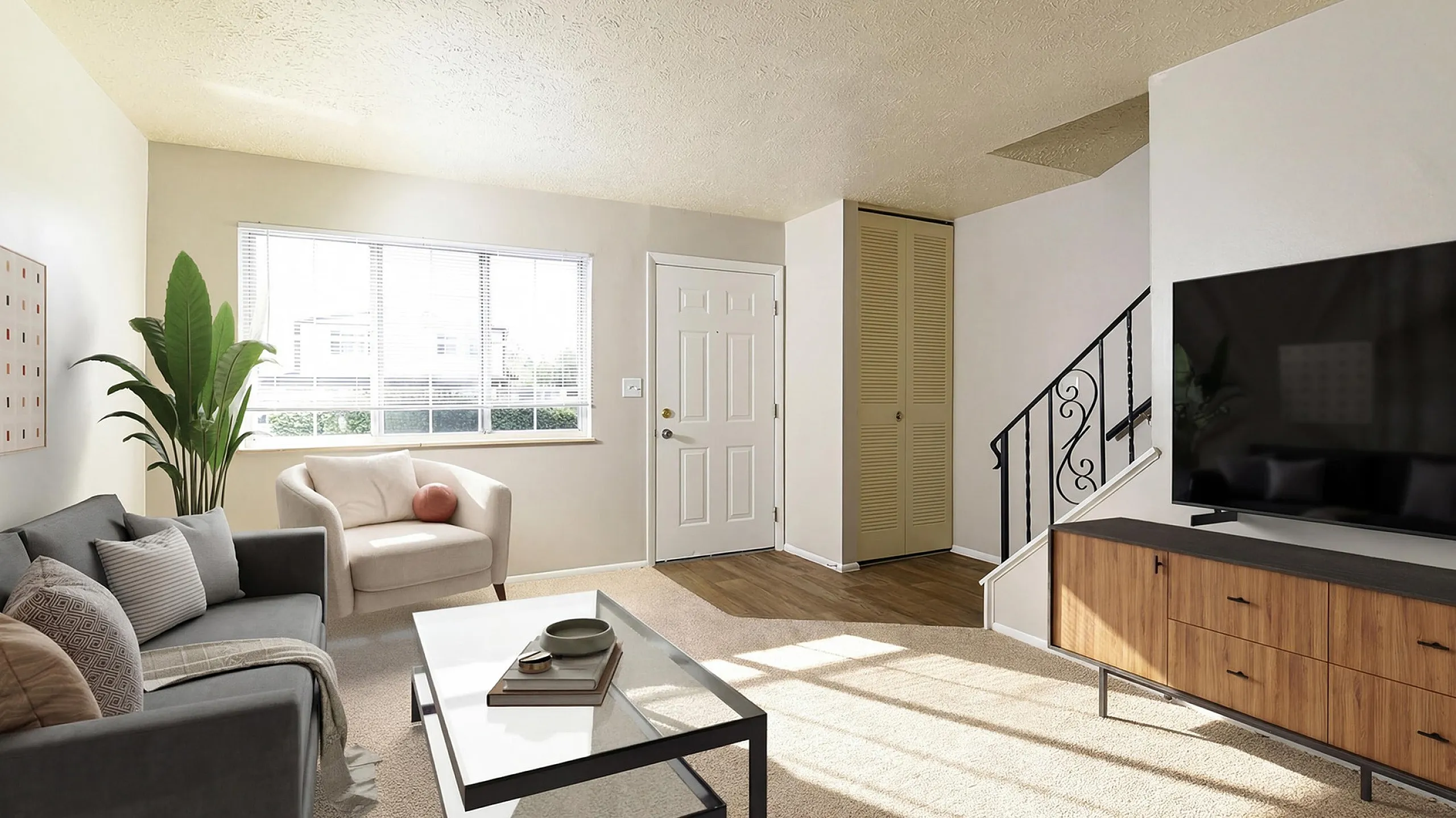 Bright and inviting living room with modern decor, featuring a cozy gray sofa, elegant armchair, and large flat-screen TV, enhanced by abundant natural light from a wide window.