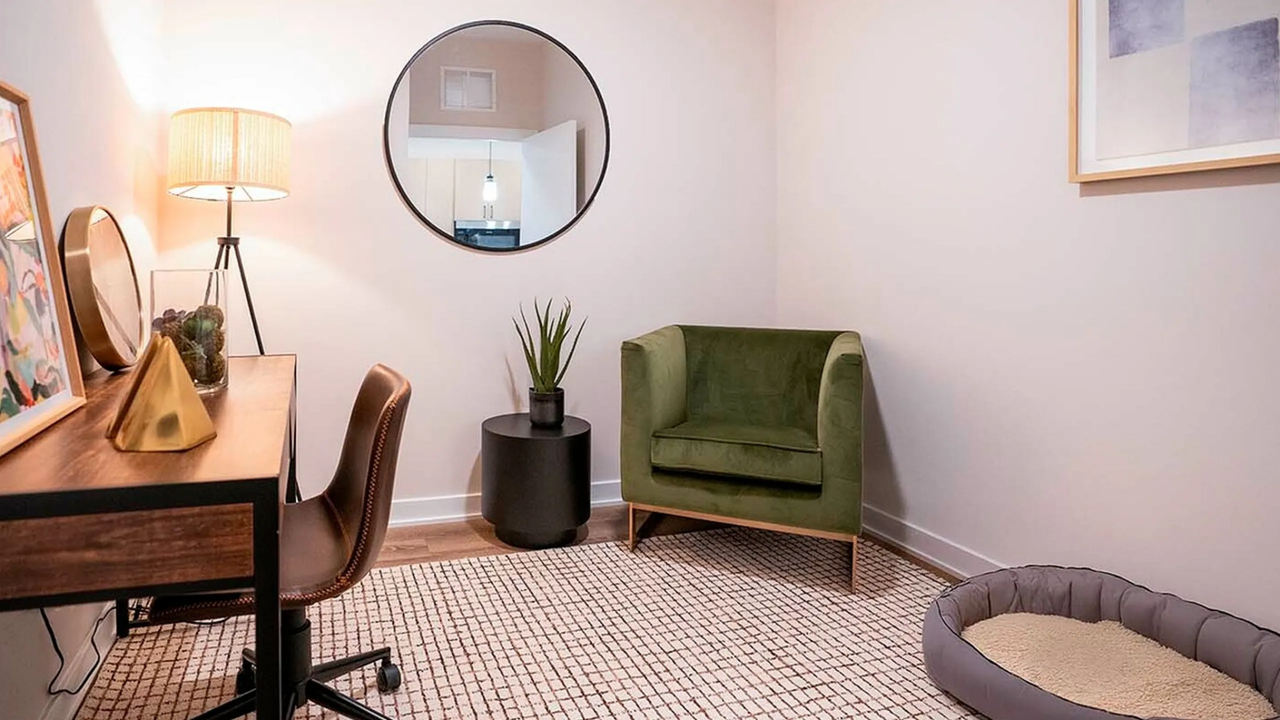 Chic home office with stylish desk, elegant green chair, modern decor, and cozy pet bed on a patterned rug.