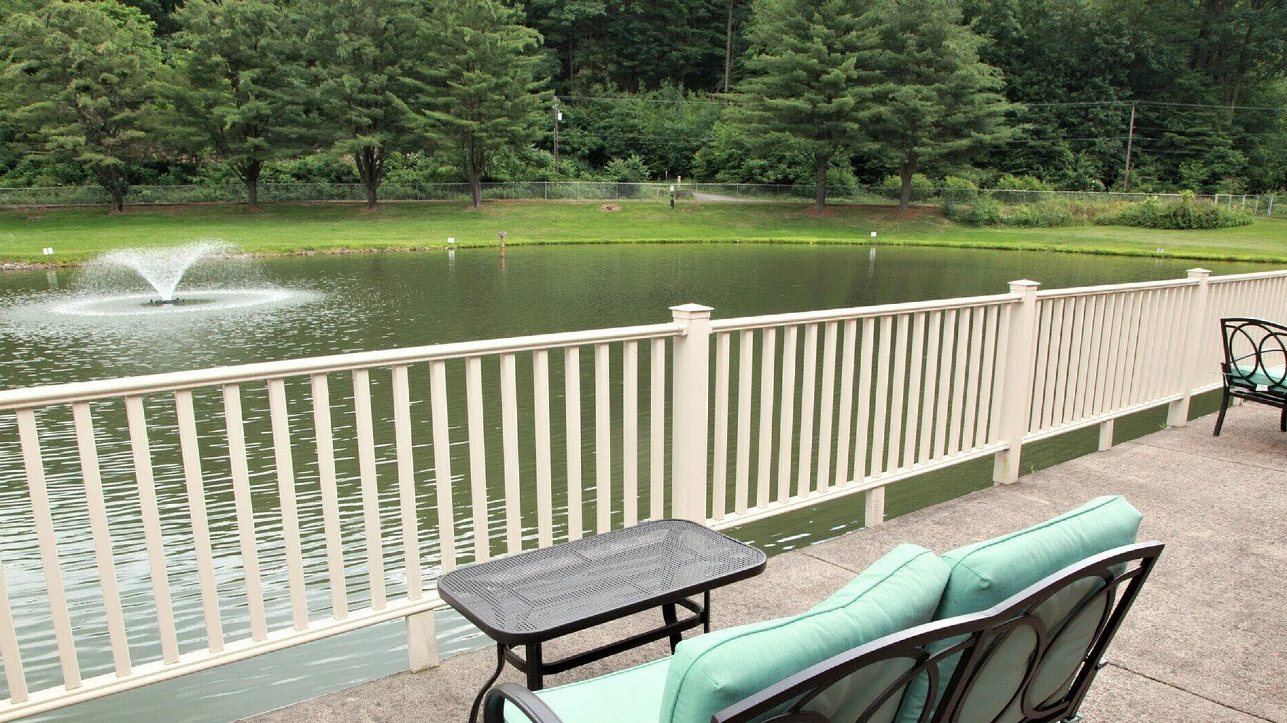 Charming outdoor patio with elegant seating overlooking a serene pond and fountain, surrounded by lush greenery.