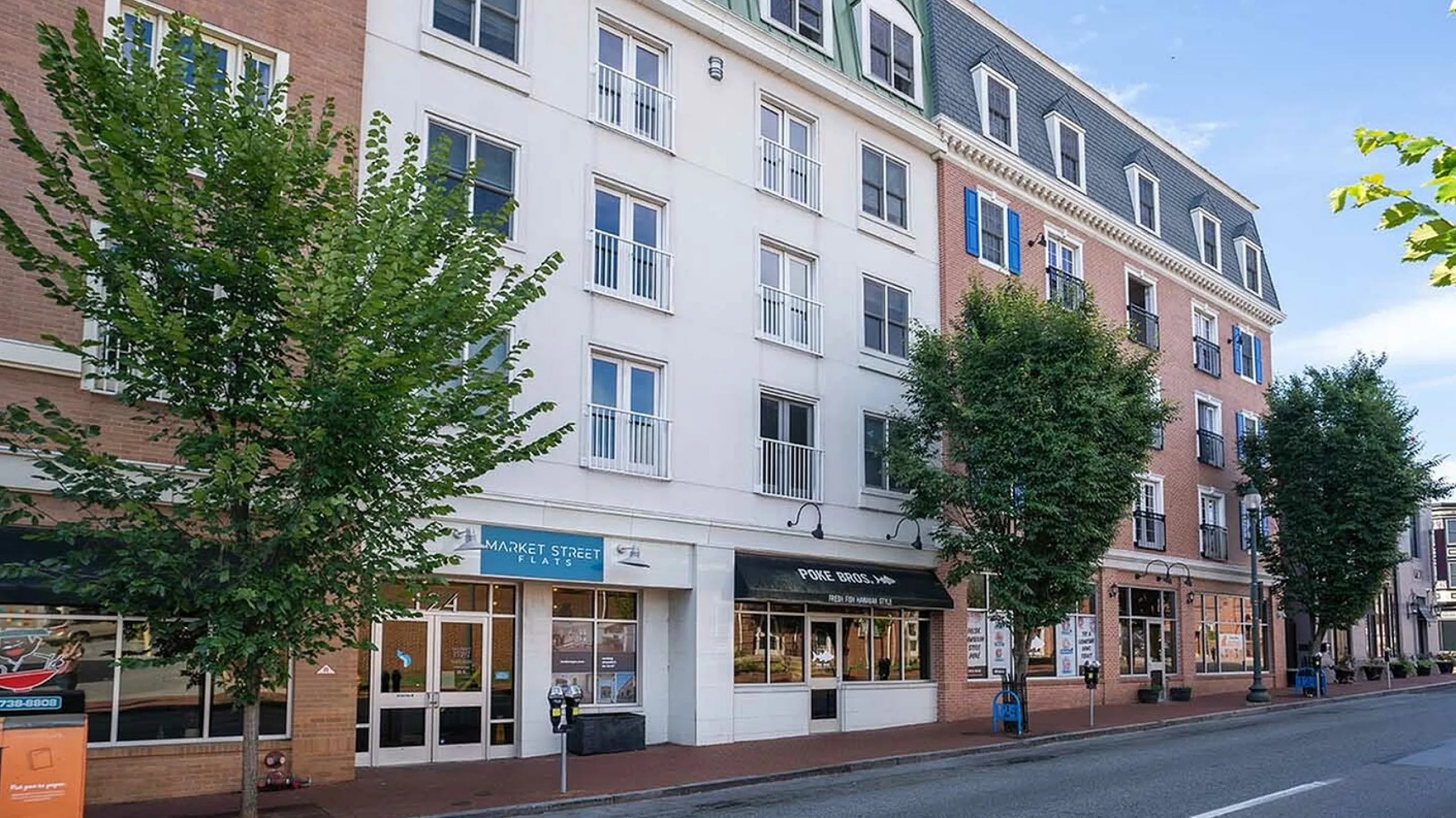 Charming urban apartment building with modern architecture, featuring street-level retail spaces and lush trees along the sidewalk.
