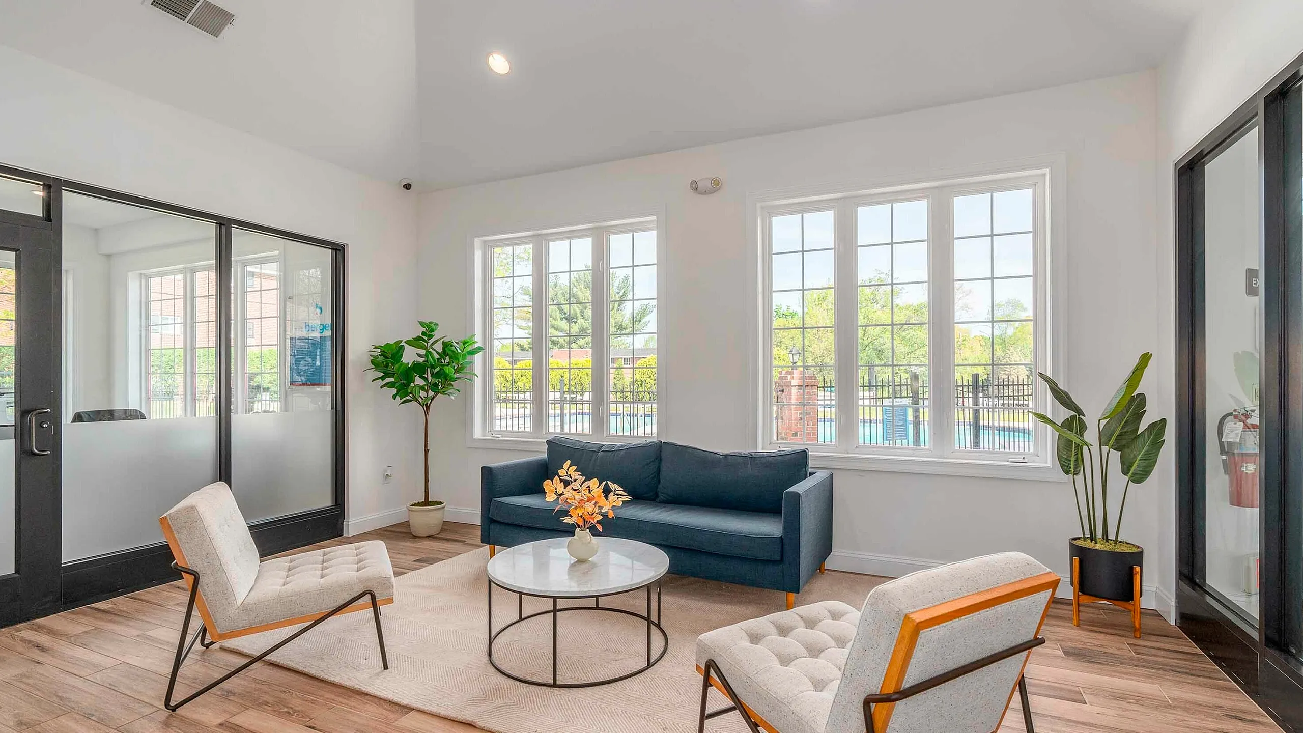 Inviting living room with elegant wood flooring, modern seating, large windows, and vibrant greenery, offering a bright and comfortable space.