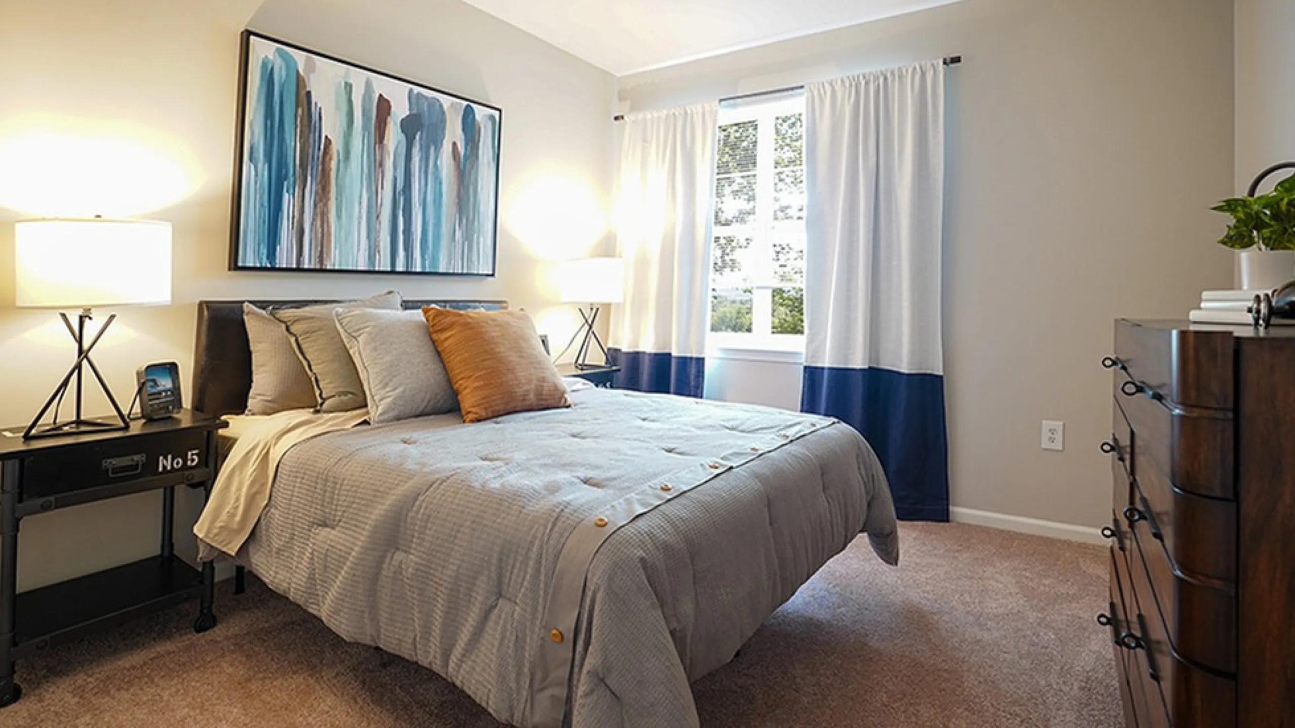 Cozy bedroom with elegant decor, featuring a plush bed, artistic wall painting, and natural light streaming through large windows.