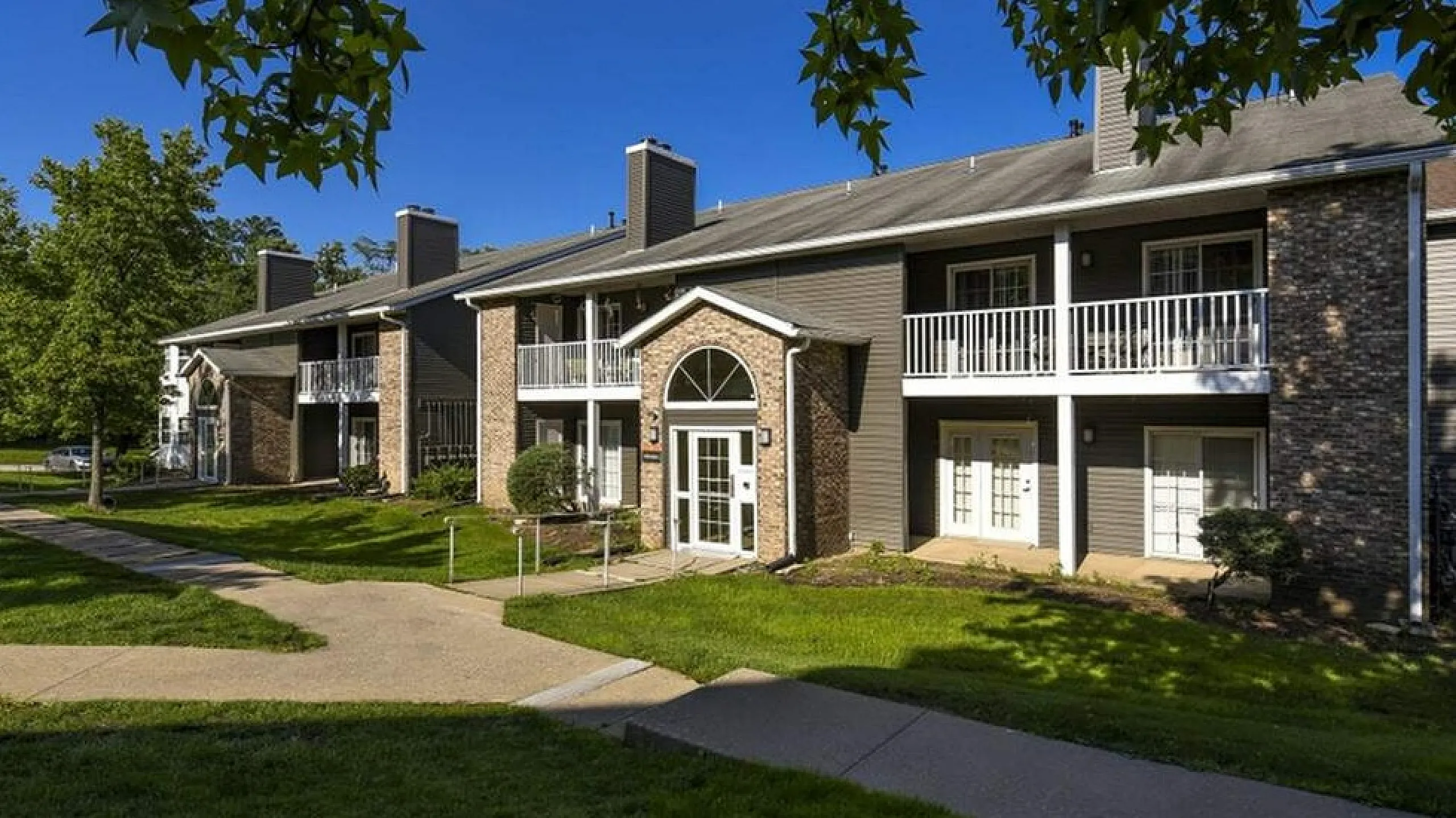 Charming duplex with brick facade and private balconies set amidst lush greenery, offering tranquil suburban living.