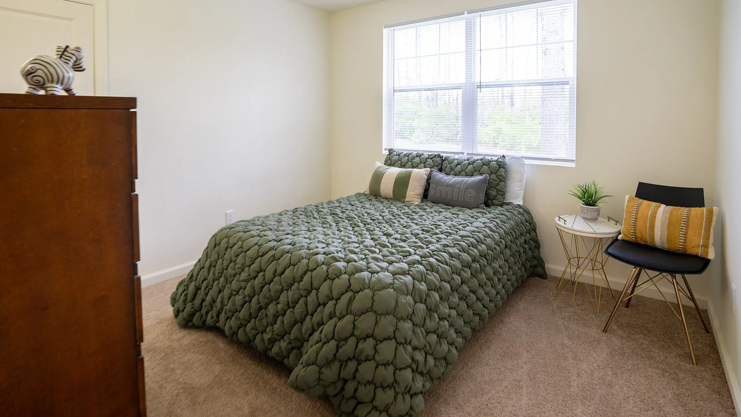 Cozy bedroom featuring a plush green comforter, stylish furniture, and abundant natural light.