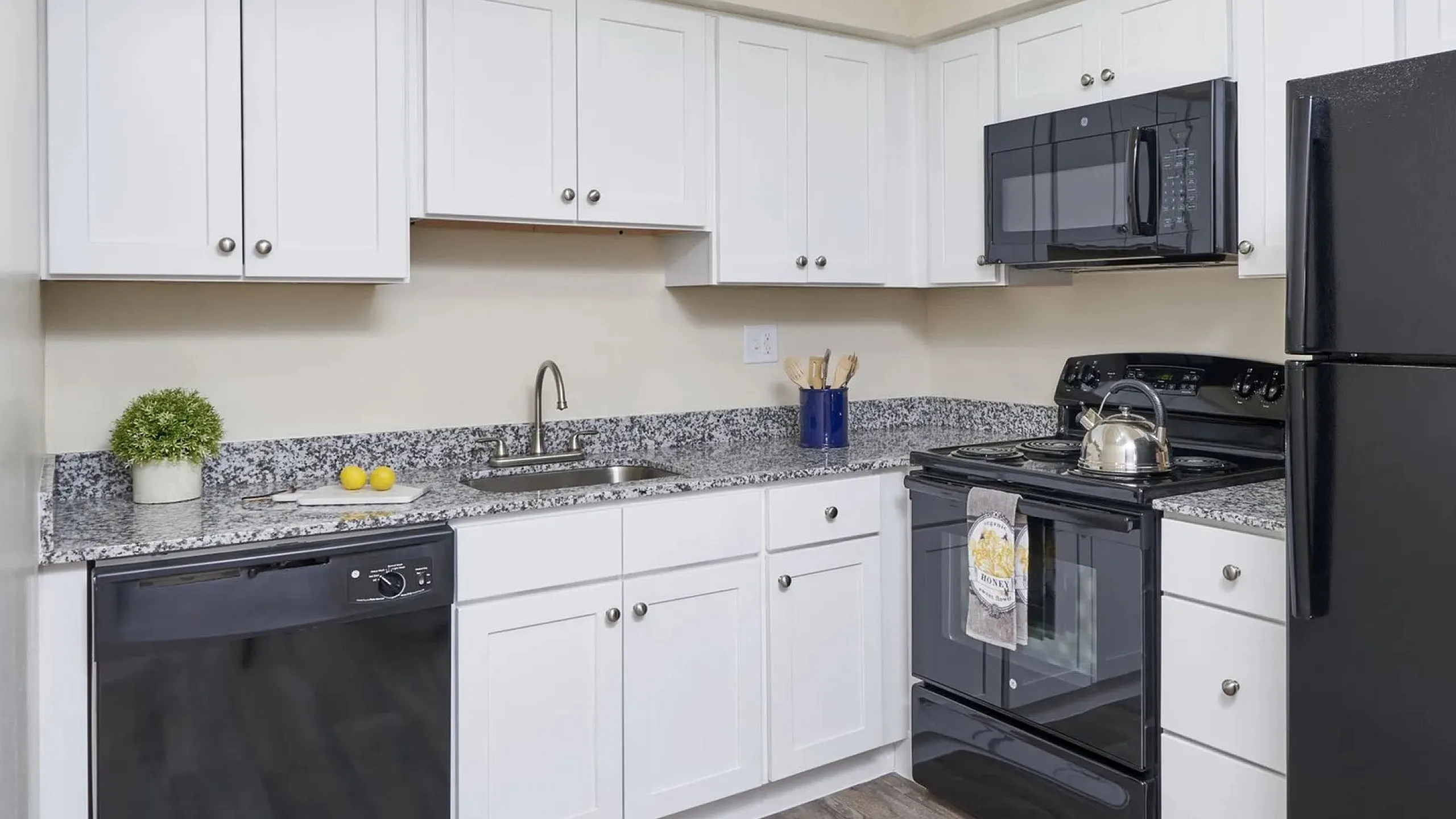 Modern kitchen with sleek black appliances, white cabinetry, granite countertops, and stylish lighting.