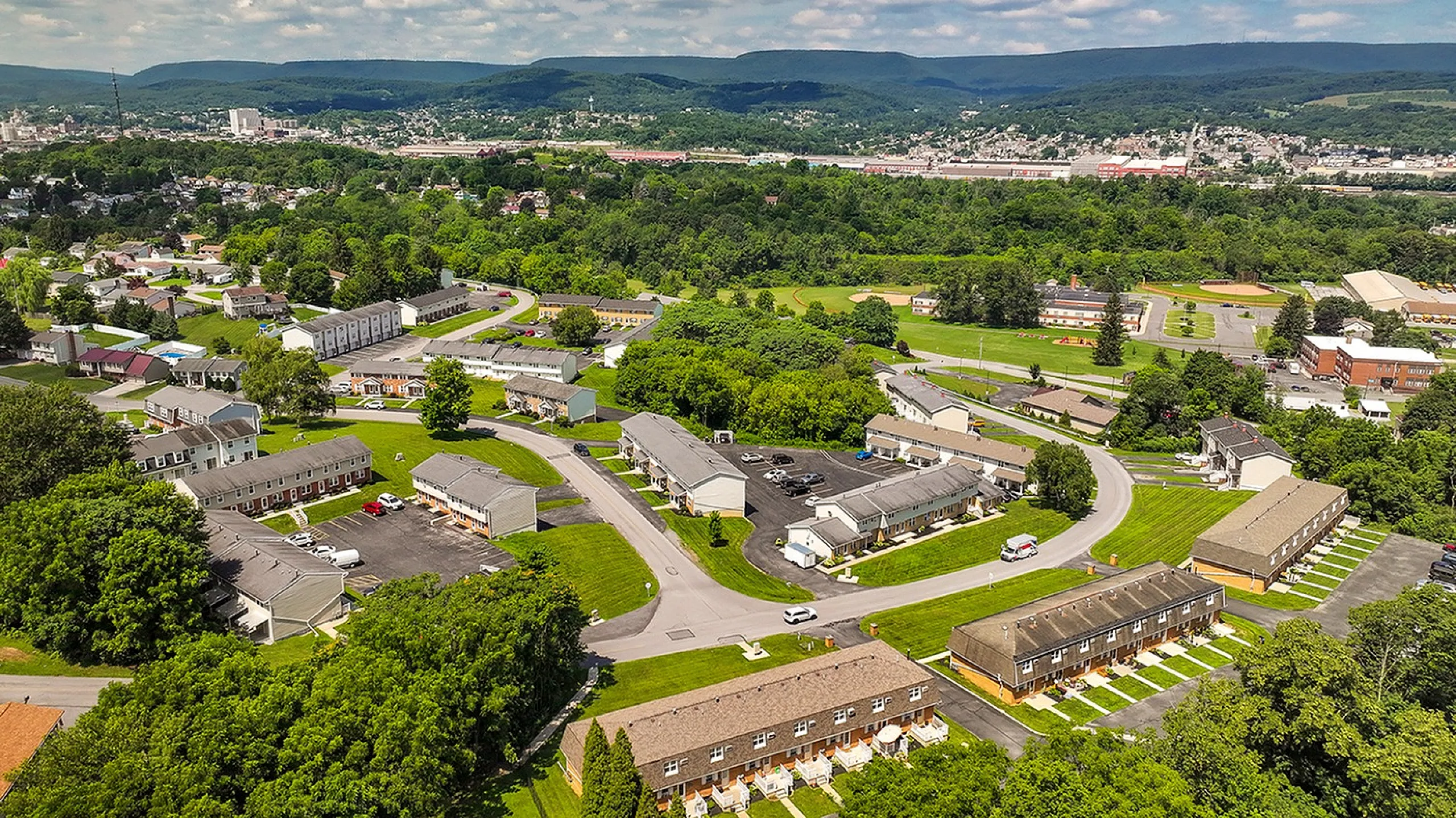 Captivating aerial view of a lush, green residential neighborhood surrounded by rolling hills; ideal for tranquil living.