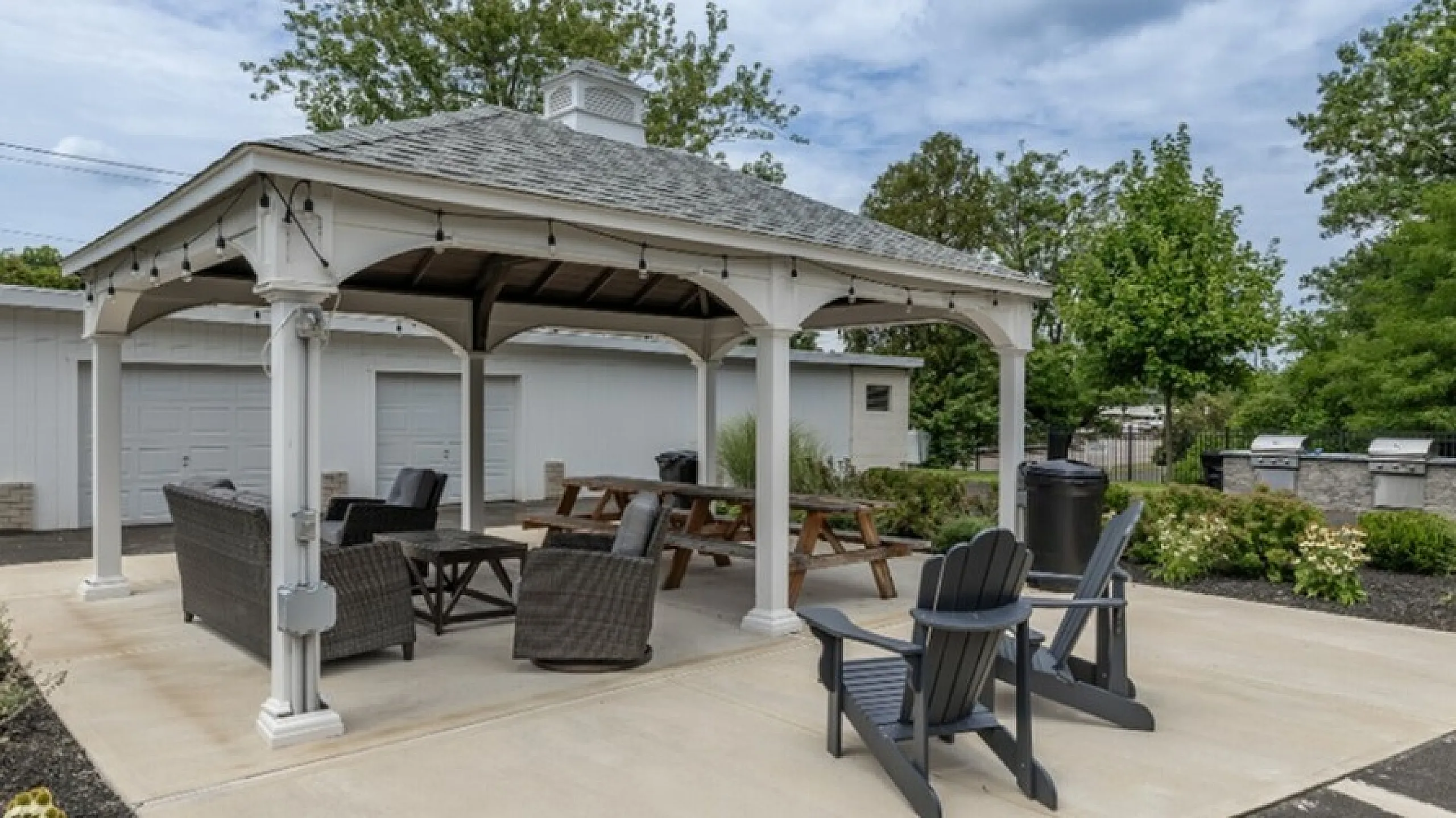Charming outdoor gazebo with cozy seating area, surrounded by lush greenery and equipped with modern BBQ grills.