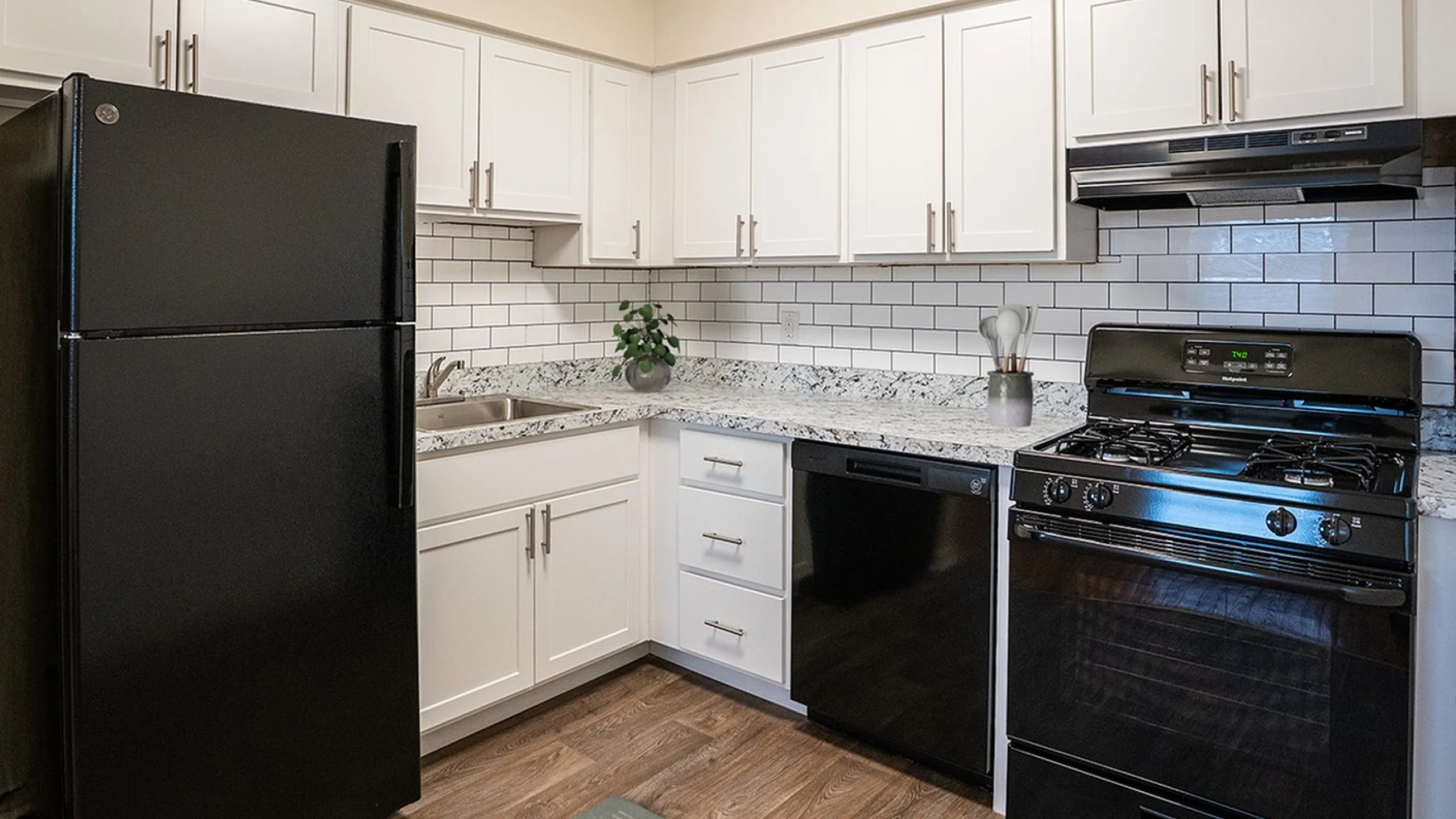 Modern kitchen with sleek black appliances, white cabinetry, and elegant granite countertops.