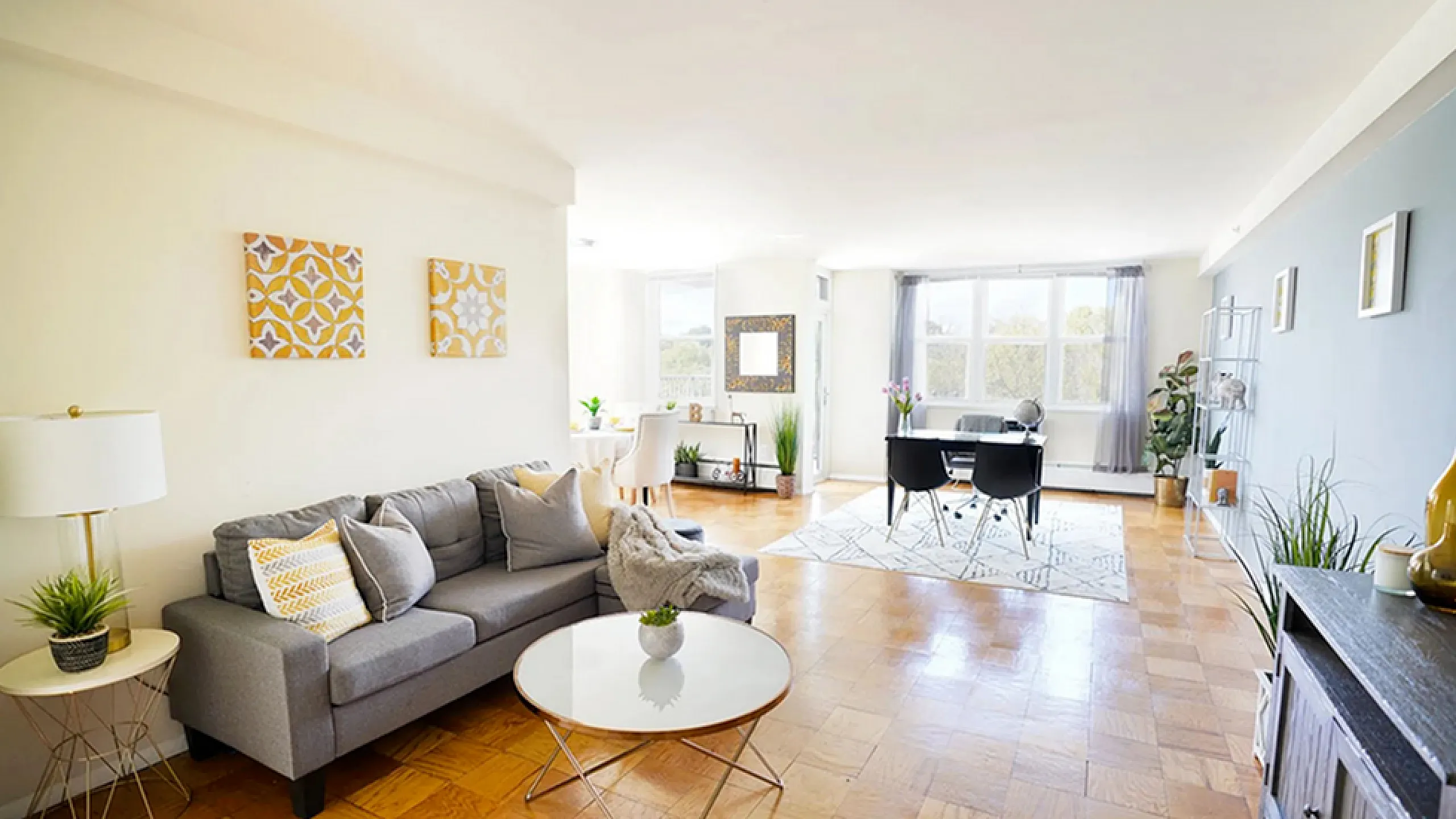 Bright and spacious living room with modern decor, featuring a cozy gray sofa, elegant parquet floors, and a stylish workspace by large sunlit windows.