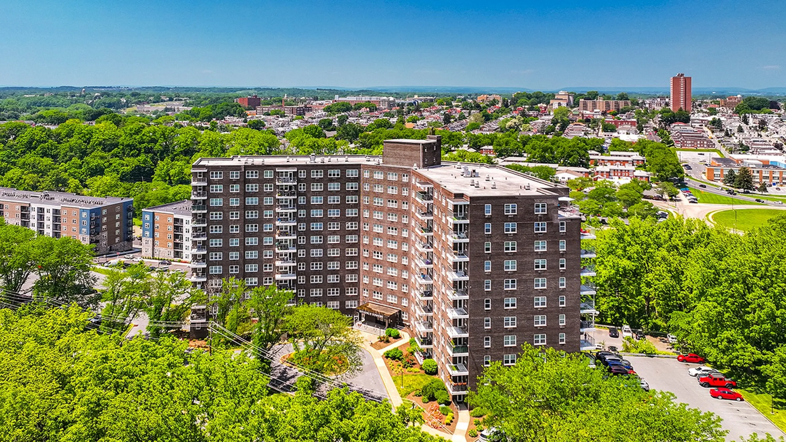 Stunning aerial view of a modern apartment building surrounded by lush greenery and a vibrant cityscape, offering convenient urban living.