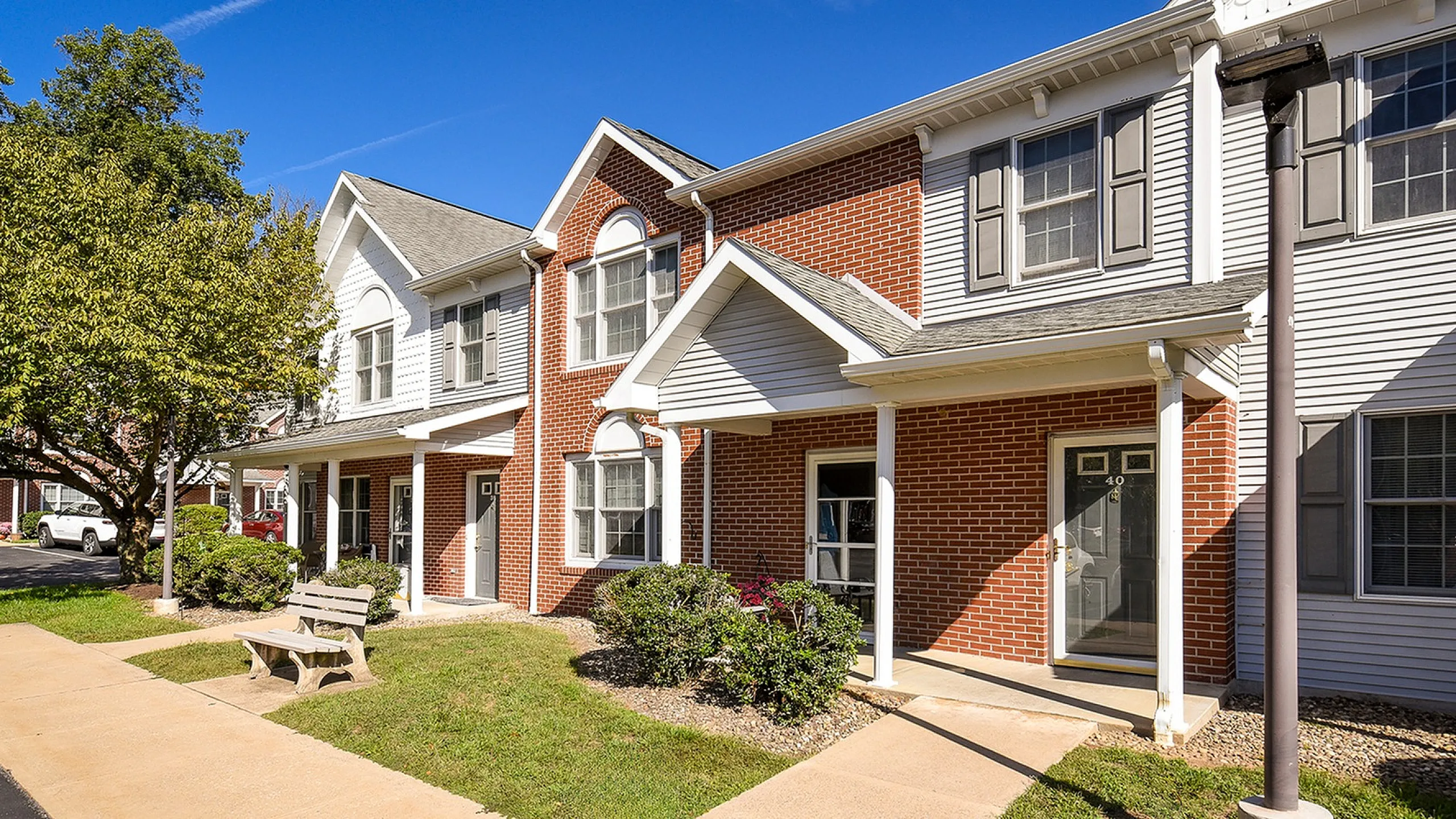 Charming townhouse with red brick and white siding exterior, featuring a cozy porch and lush green landscaping.