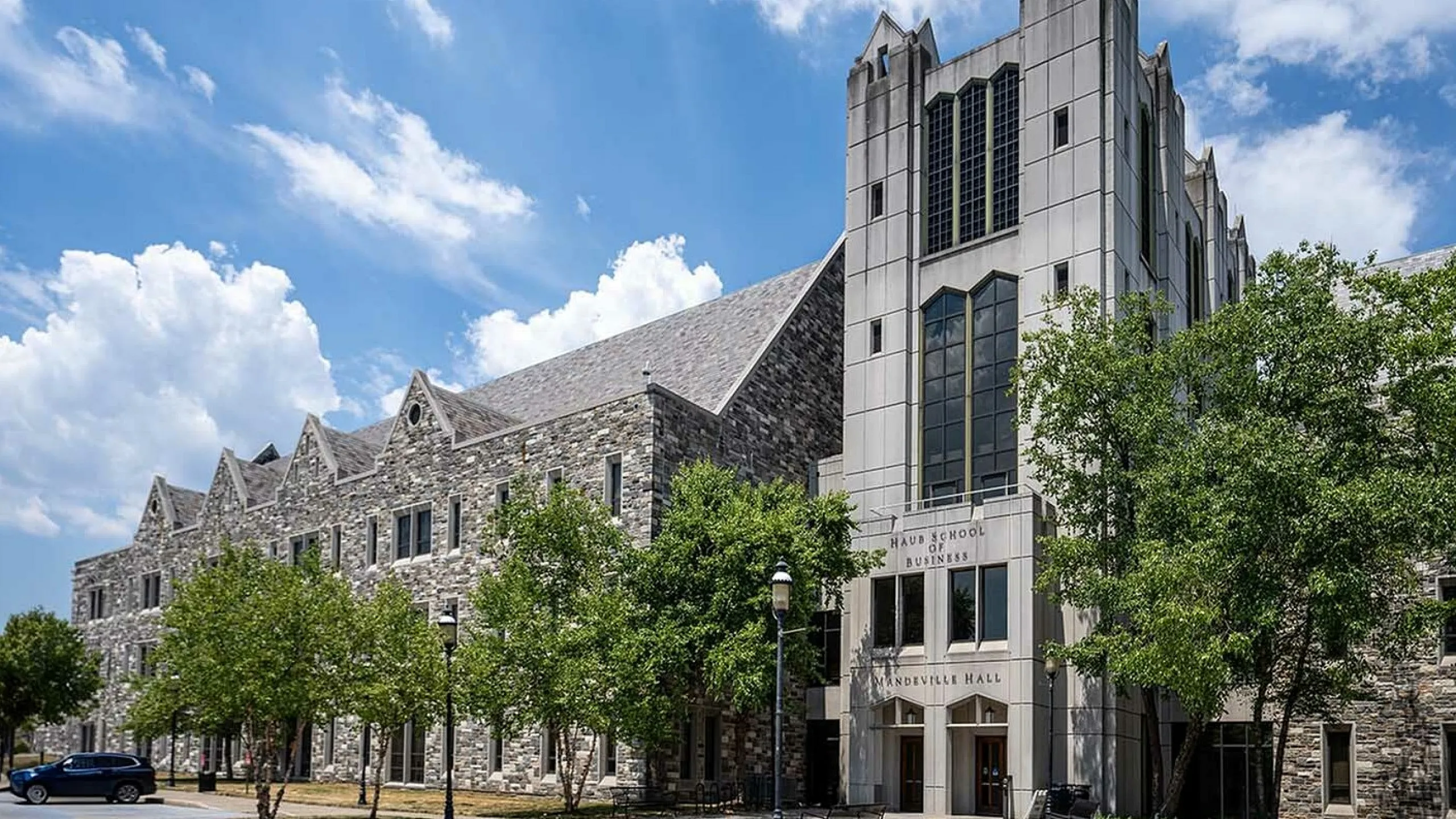 Elegant stone building with Gothic architecture surrounded by lush trees under a vibrant blue sky.