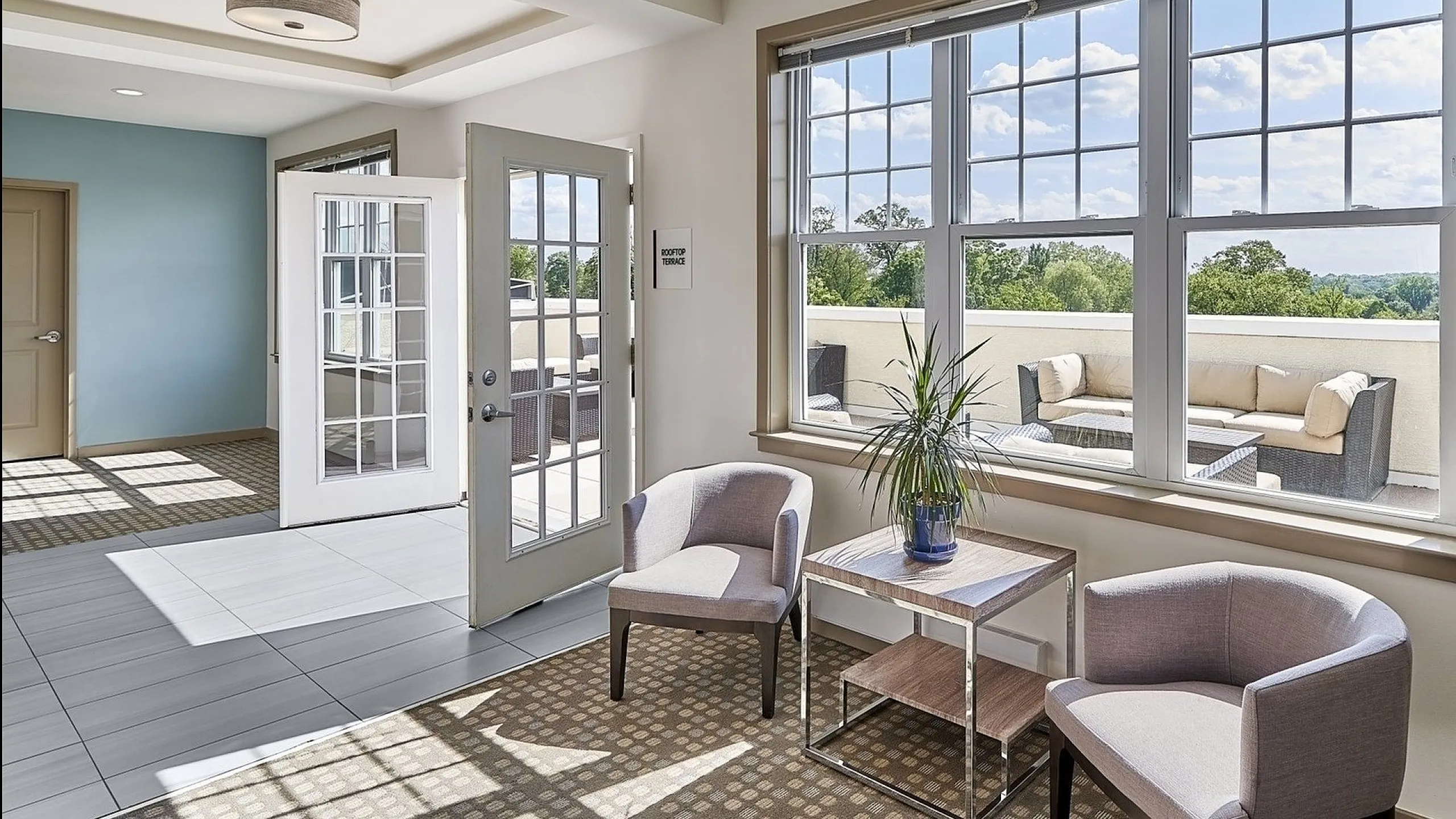 Bright apartment with large windows, cozy chairs, and access to a spacious rooftop terrace with lush views.