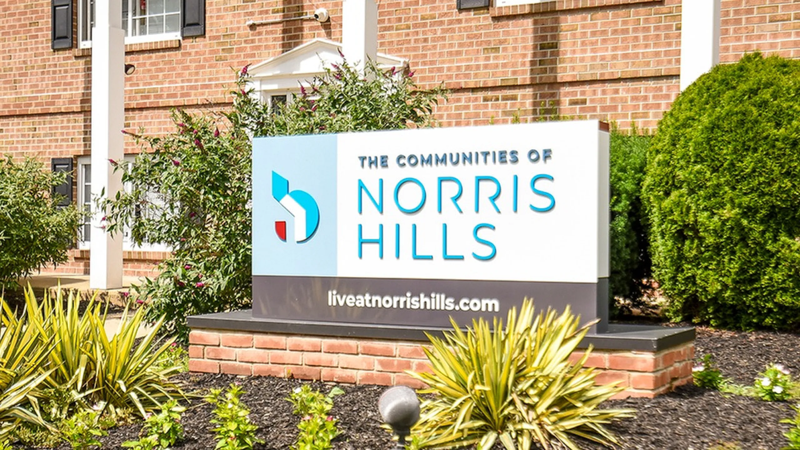 Inviting entrance of The Communities of Norris Hills with lush greenery and bold signage.