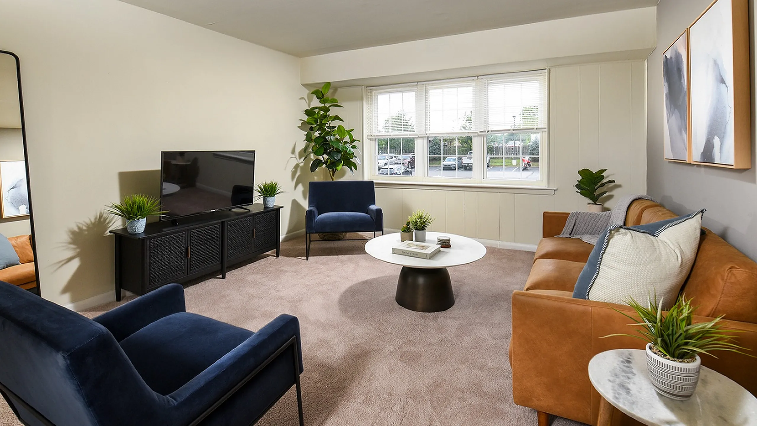 Inviting living room with modern decor featuring a plush leather sofa, chic blue armchairs, and a stylish coffee table. Large windows brighten the space with natural light.