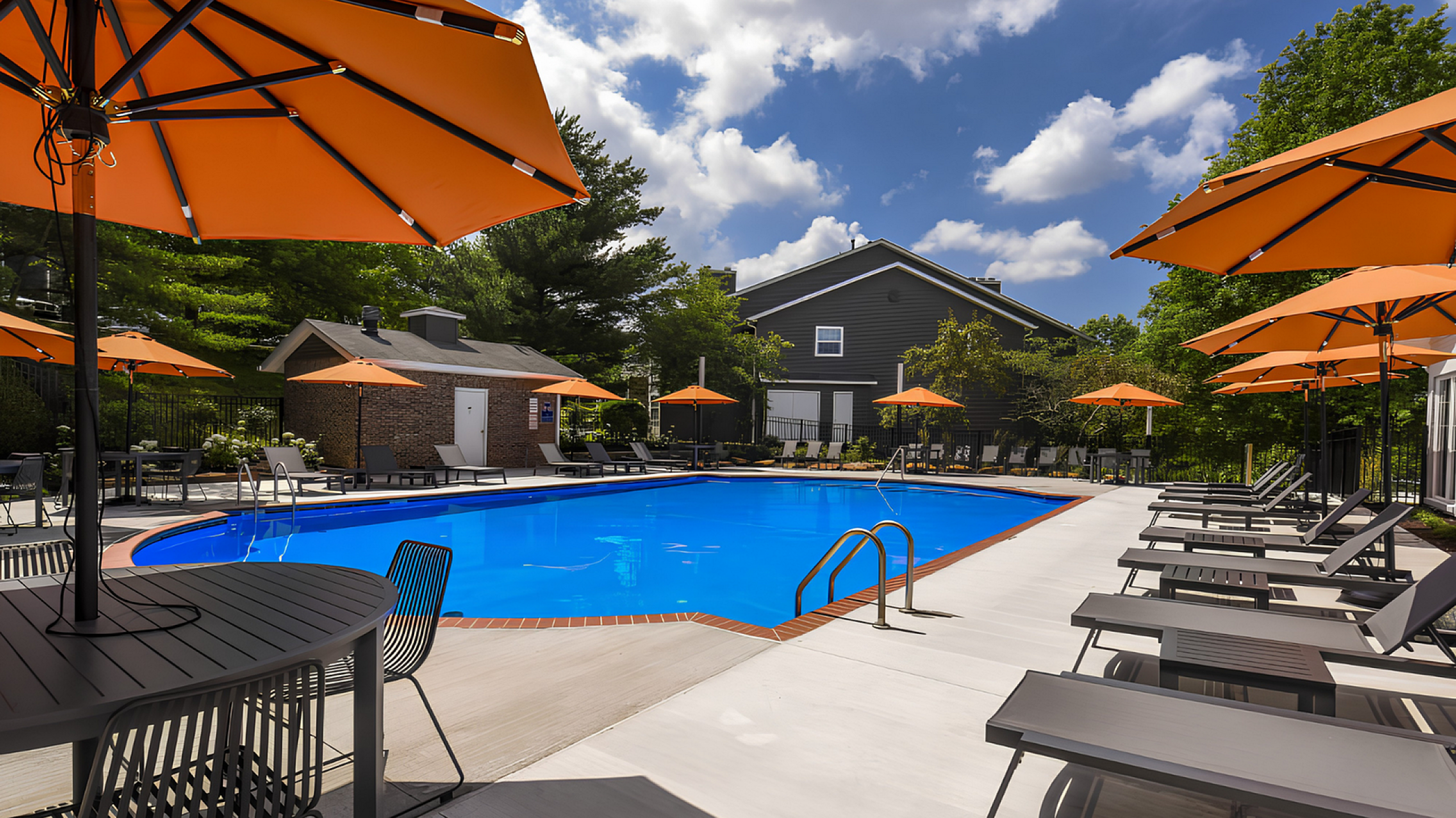 Inviting outdoor pool area with vibrant orange umbrellas, modern lounge chairs, and lush greenery under a bright blue sky.