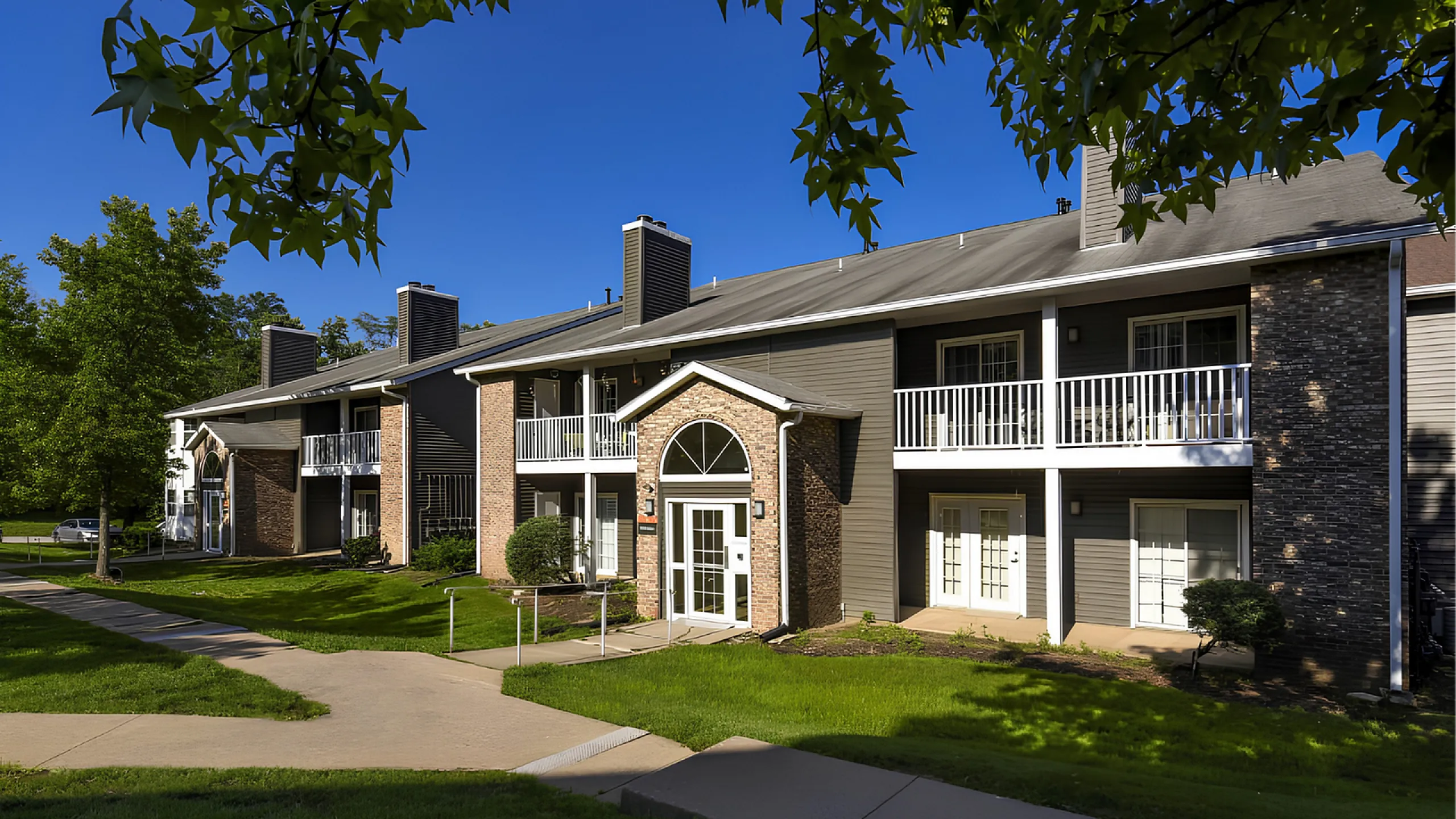 Charming apartment complex with elegant balconies, lush greenery, and picturesque entryways under a bright blue sky.