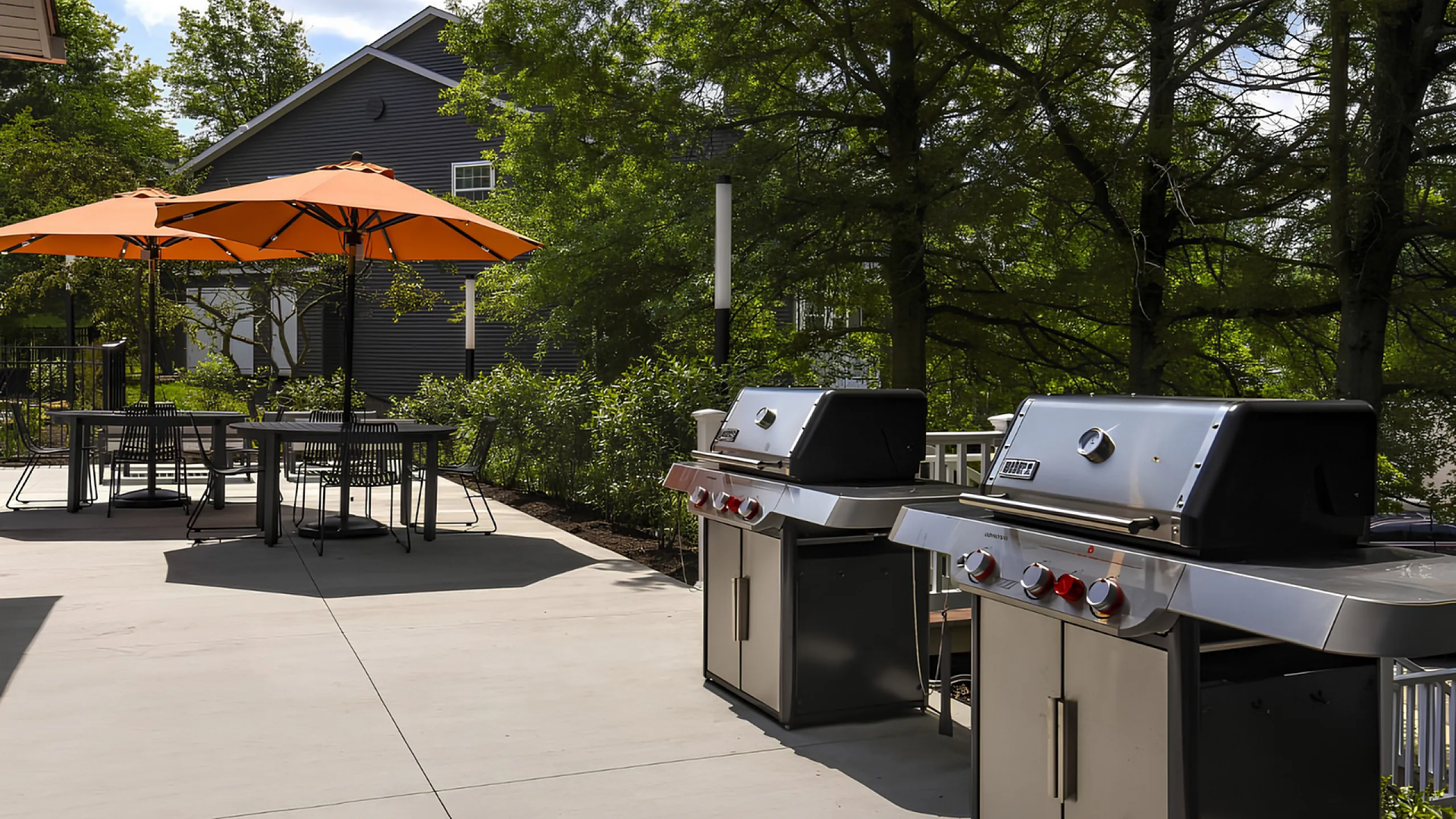 Charming outdoor patio with modern grills, vibrant orange umbrellas, and lush greenery for peaceful gatherings.