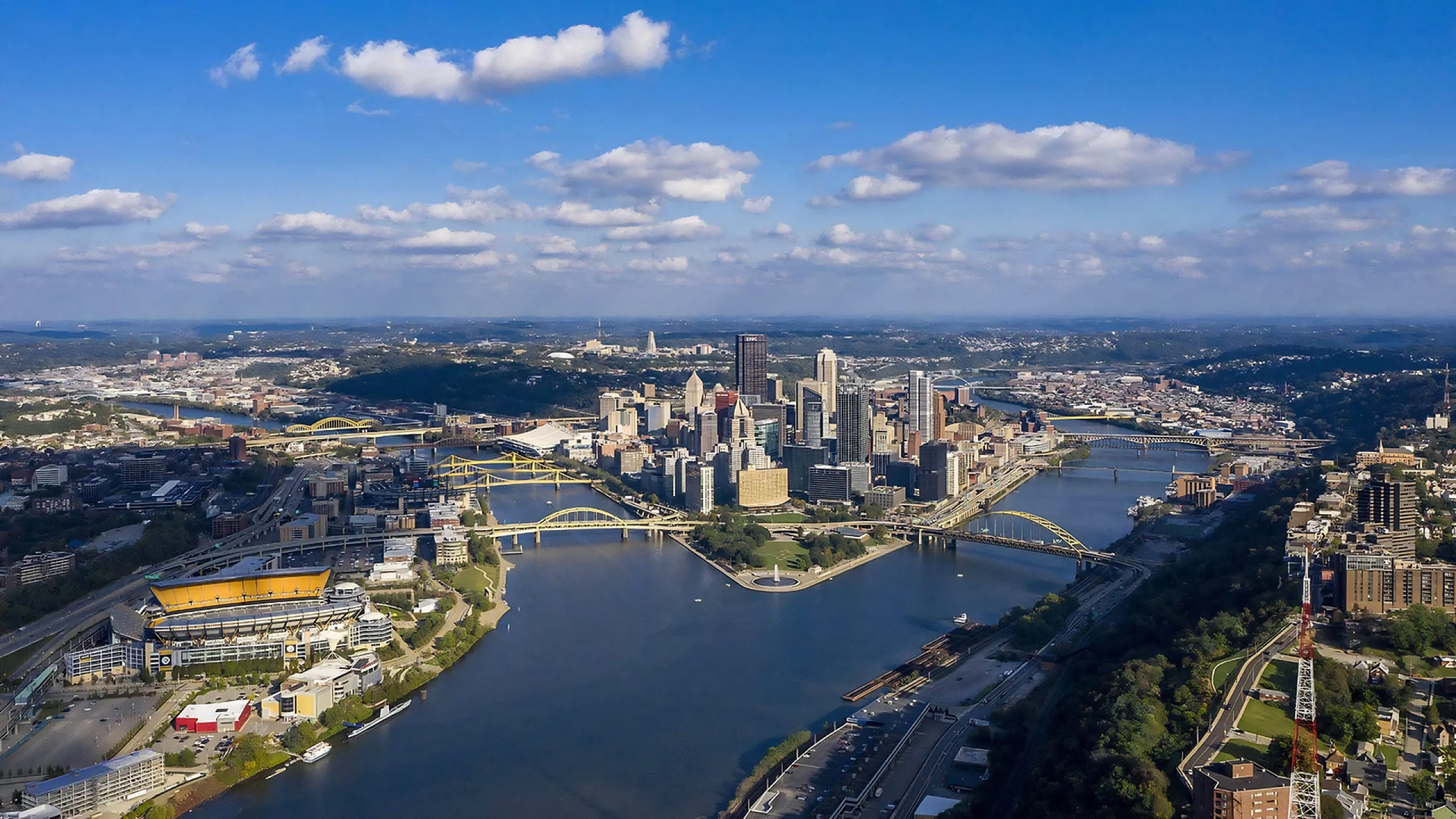 Breathtaking aerial view of a vibrant cityscape with iconic bridges spanning across a shimmering river, set under a picturesque blue sky.