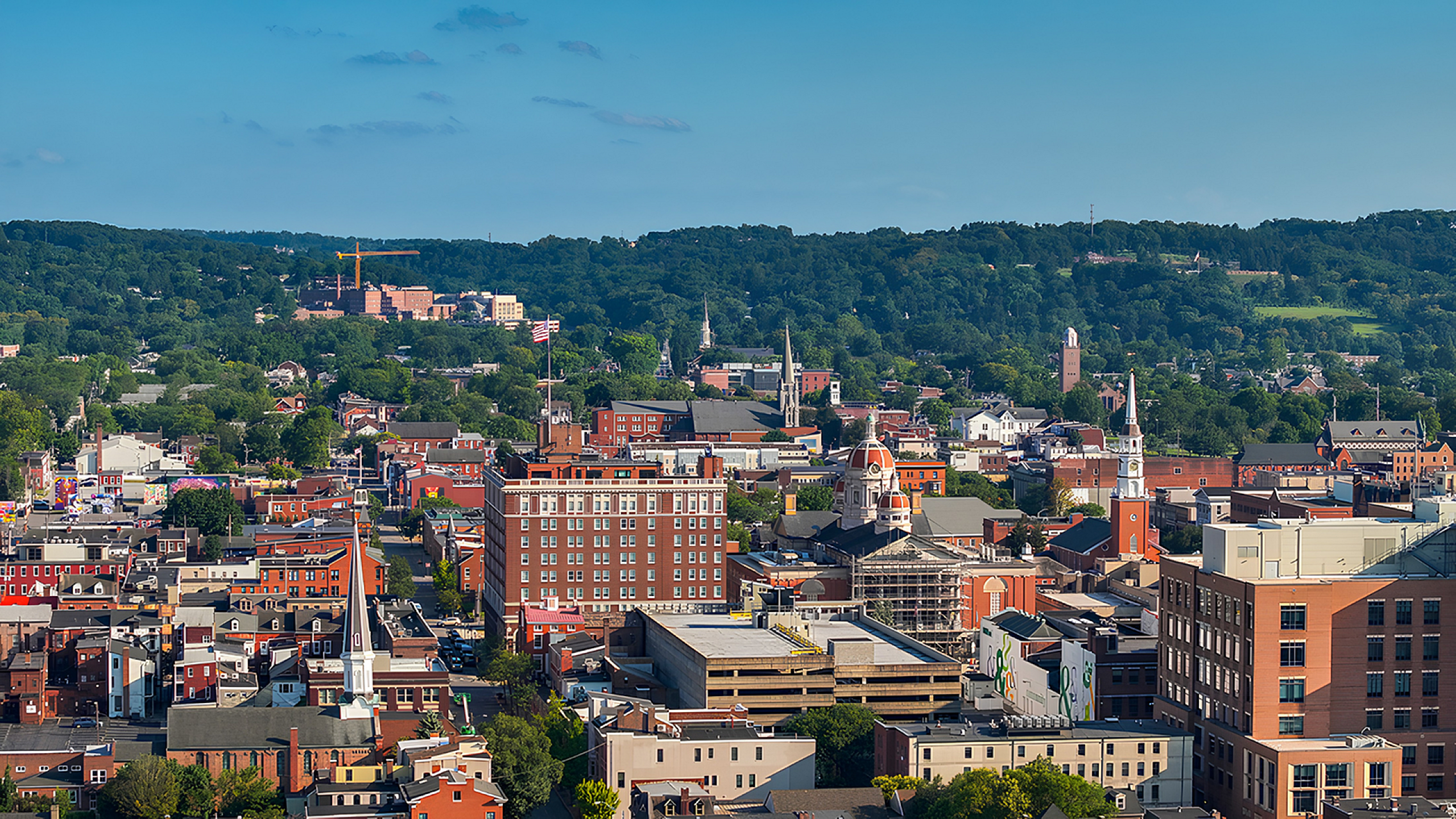 Vibrant cityscape view showcasing charming architecture and lush greenery set against a backdrop of rolling hills under a clear blue sky.
