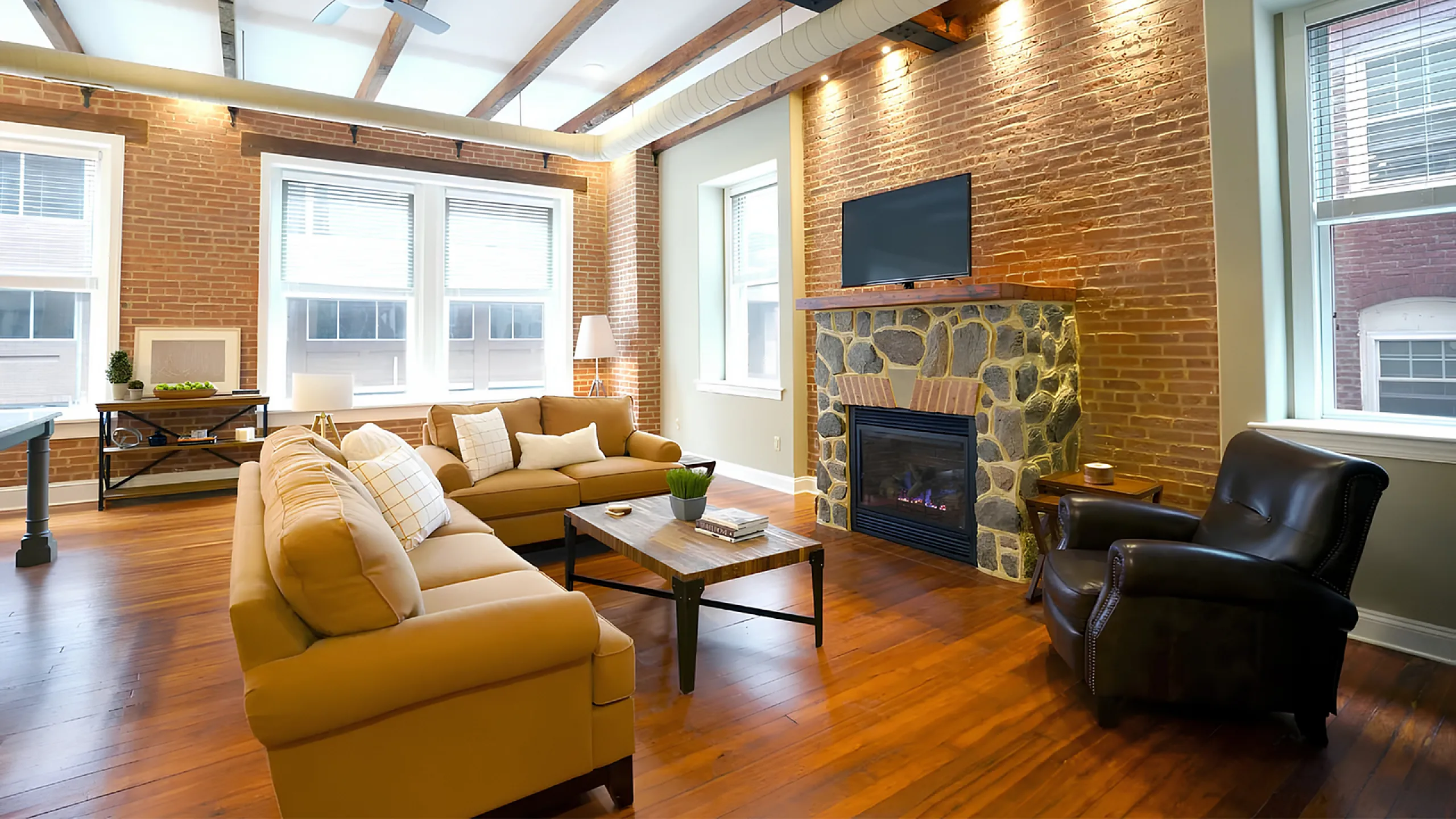 Charming living room with exposed brick walls, cozy leather sofas, and a stone fireplace creating a warm, inviting atmosphere.