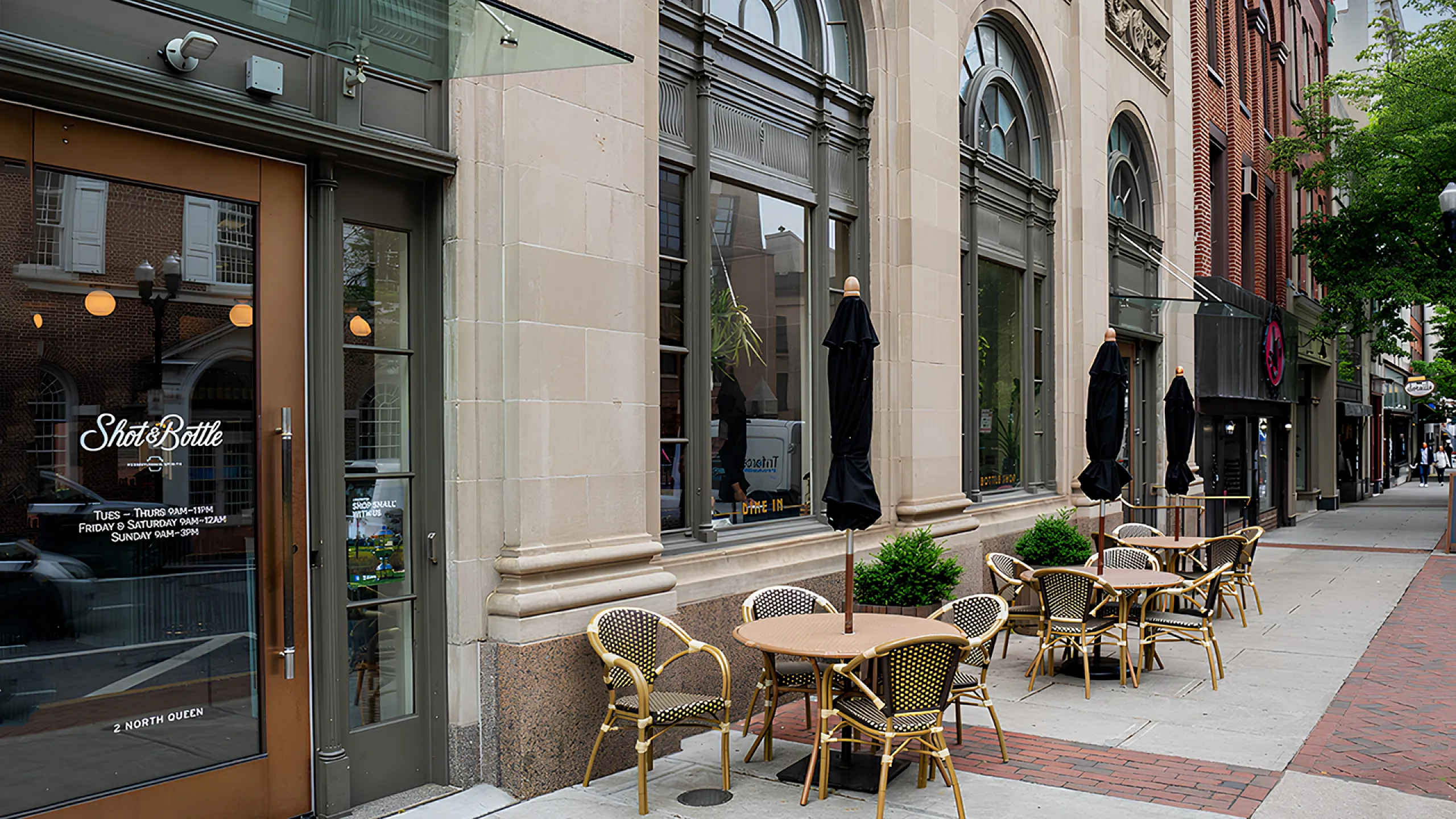 Charming street view of a stylish cafe with outdoor seating, featuring elegant chairs and tables under classic architecture.