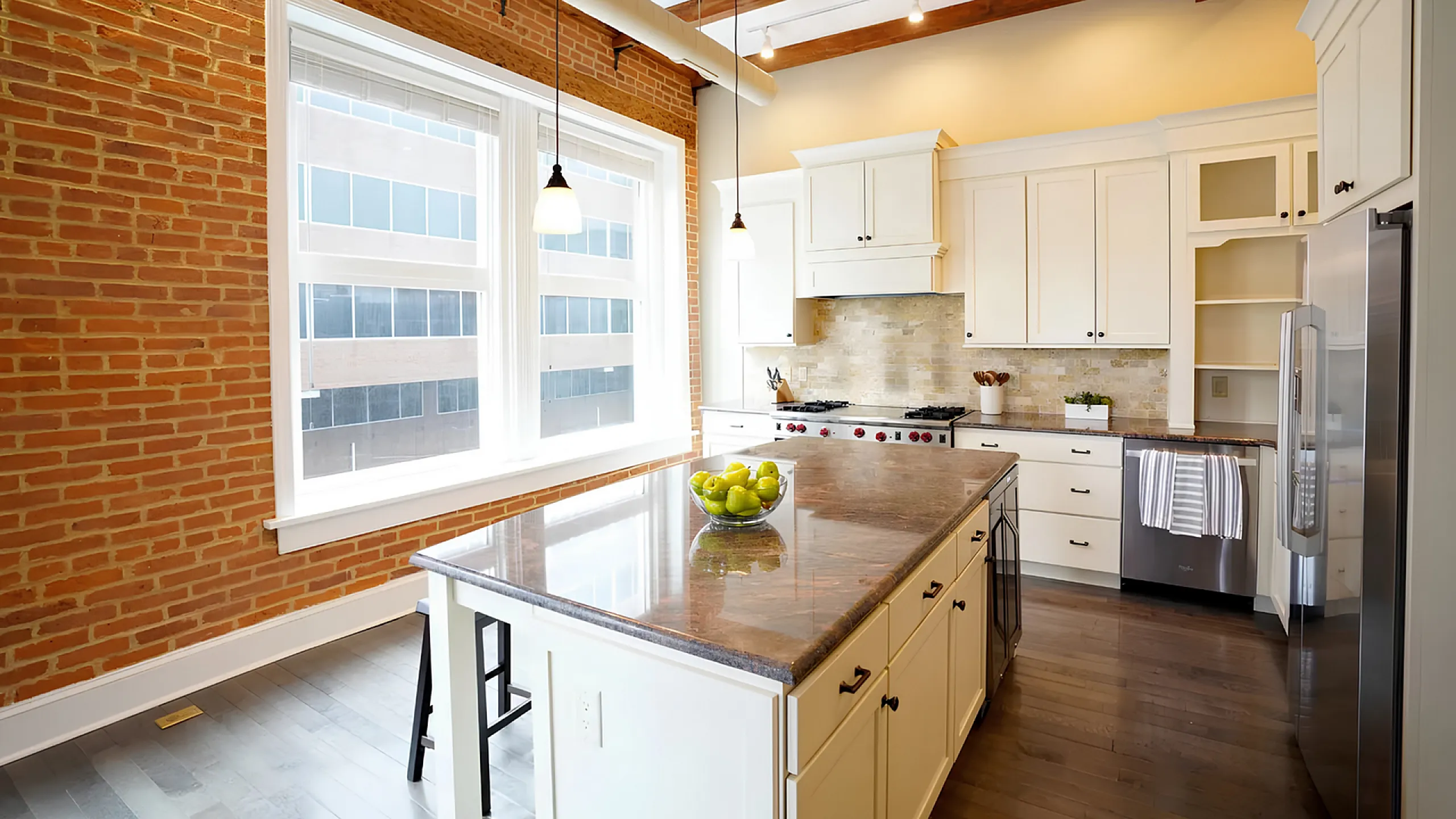 Contemporary kitchen with elegant granite island, brick accent wall, and large sunlit windows.