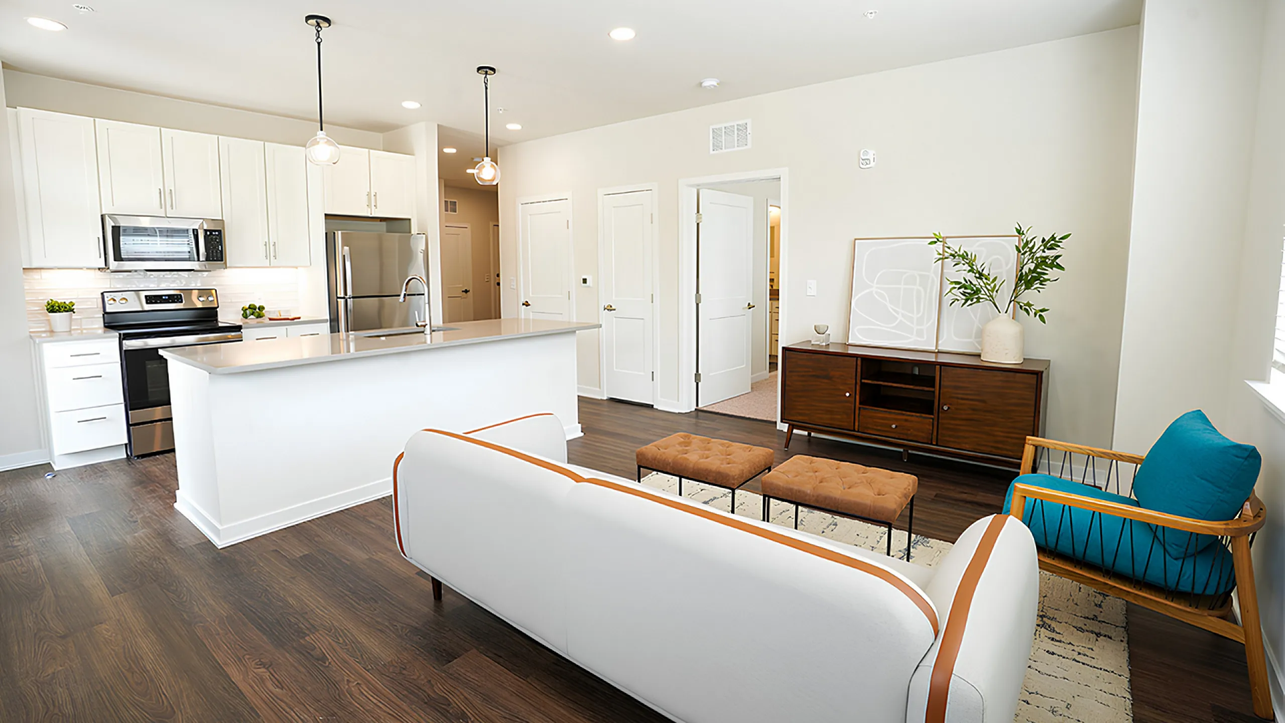 Modern open-concept living area featuring a sleek white kitchen with stainless steel appliances, cozy seating, and stylish decor.