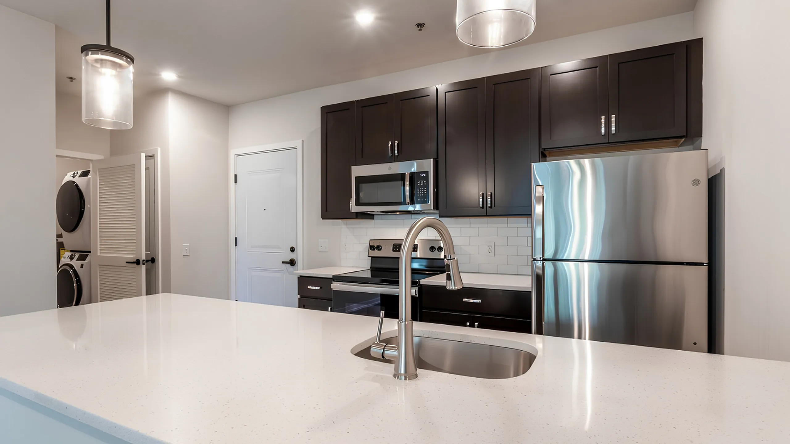 Sleek modern kitchen with stainless steel appliances, elegant dark cabinets, and a pristine white countertop, perfect for stylish living.