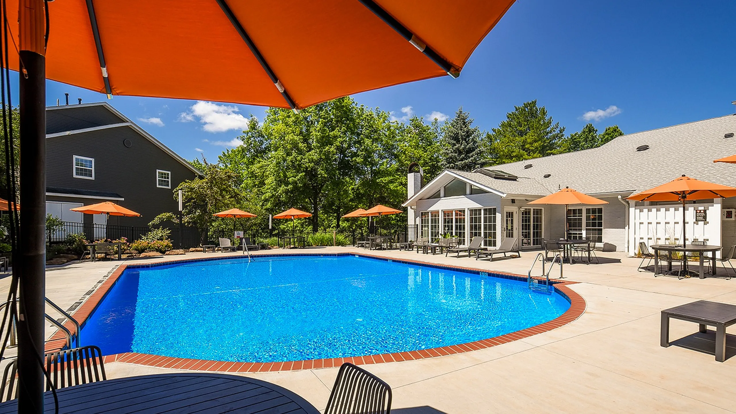 Inviting outdoor pool area with vibrant orange umbrellas, surrounded by lush greenery and modern lounge seating.