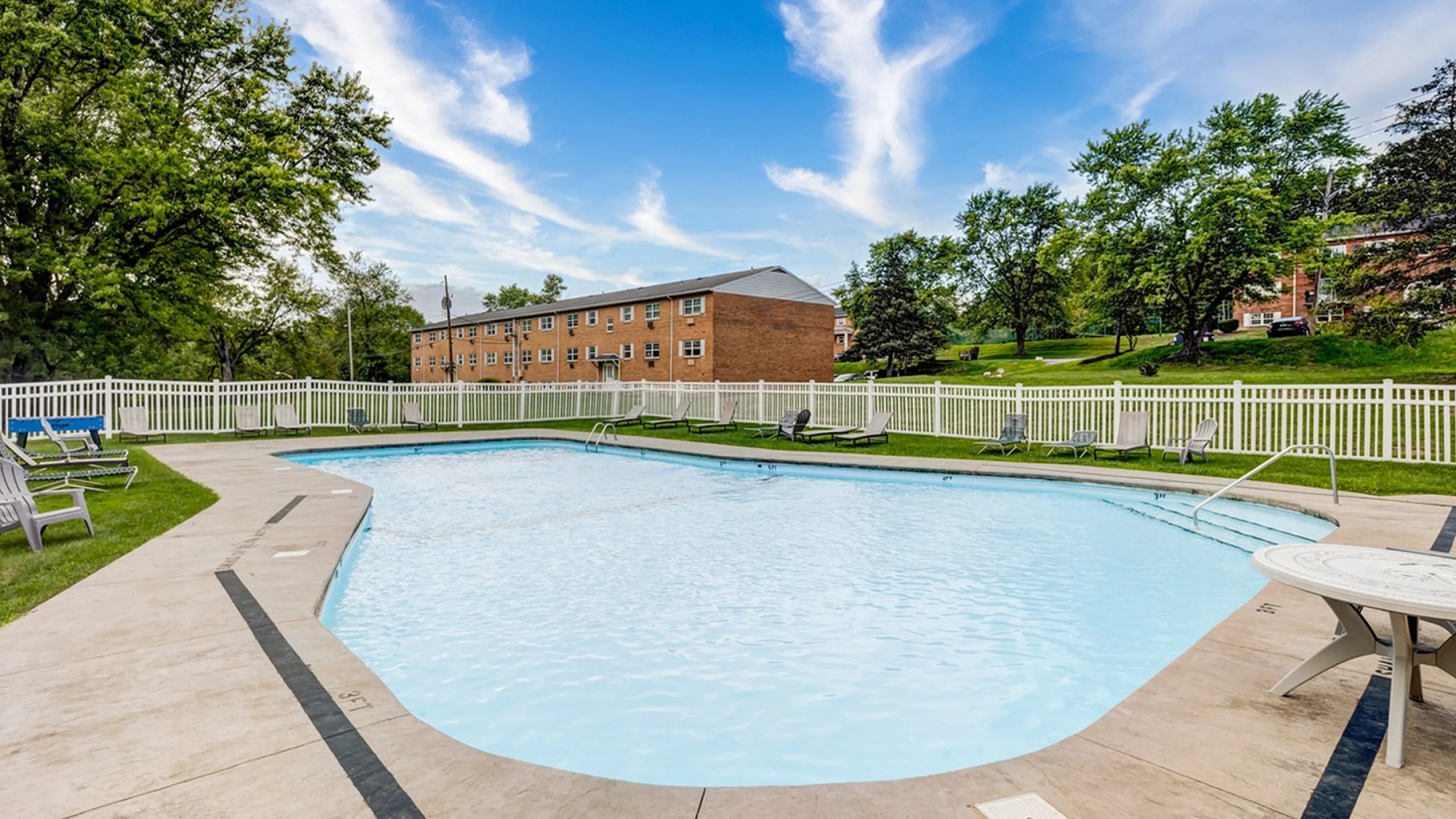 Inviting outdoor community pool surrounded by lush greenery and comfortable lounging chairs, perfect for relaxation and leisure.