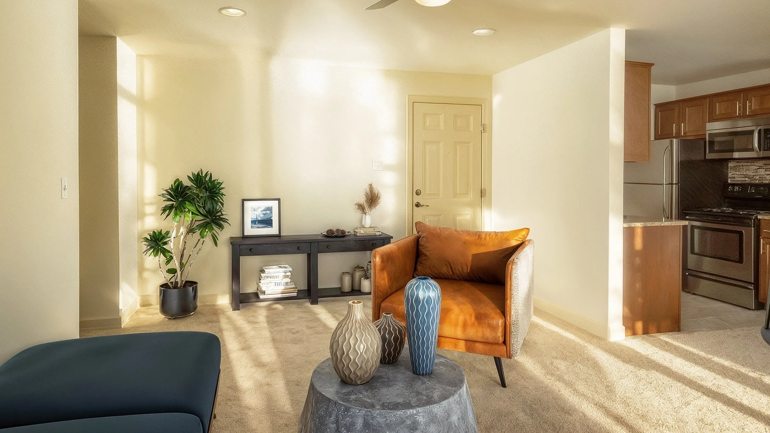 Bright and inviting living space with modern decor, featuring a cozy armchair, artistic vases, and an open-concept kitchen in the background.