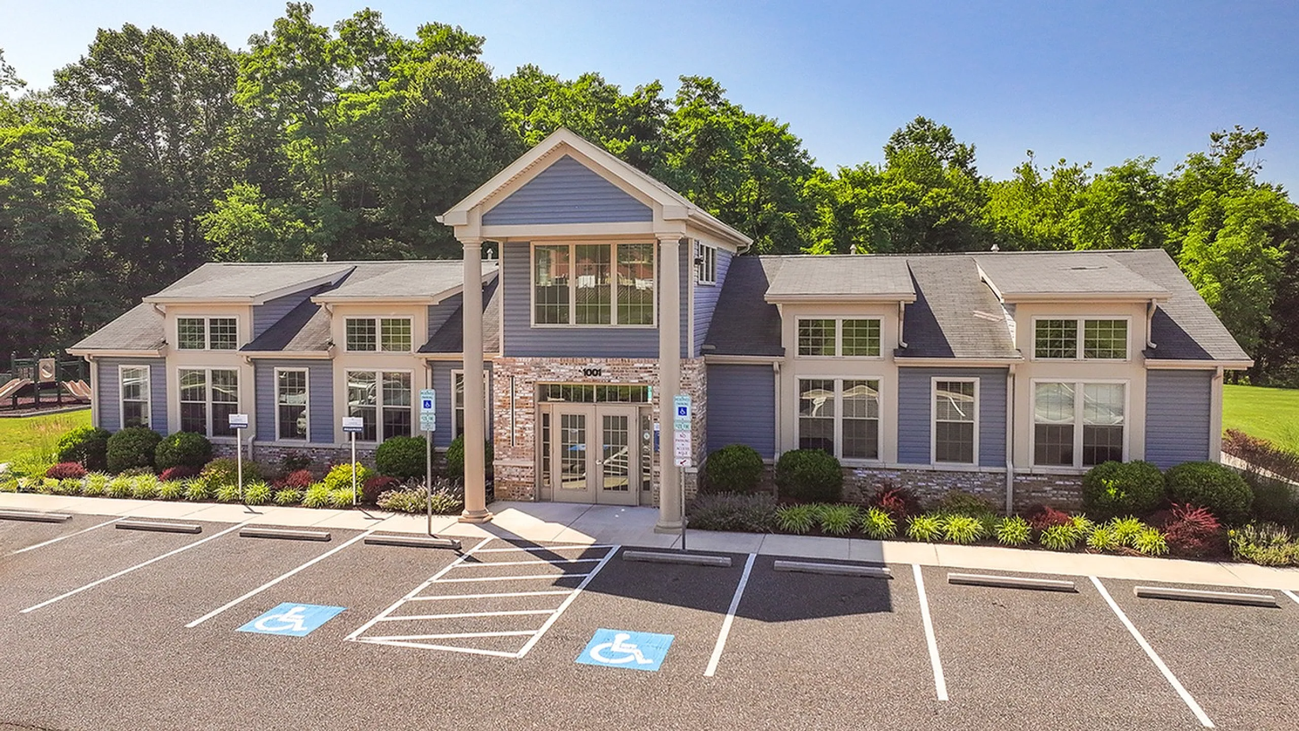 Charming residential building with a modern blue facade, surrounded by lush greenery and convenient parking spaces.