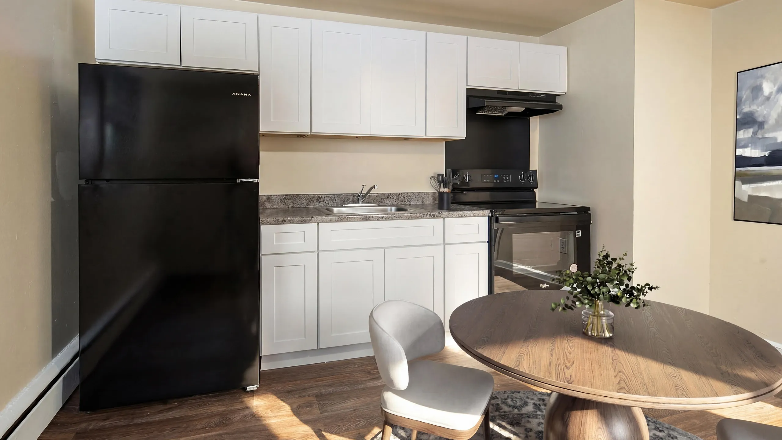Charming modern kitchen with sleek black appliances, elegant white cabinetry, and cozy dining area.