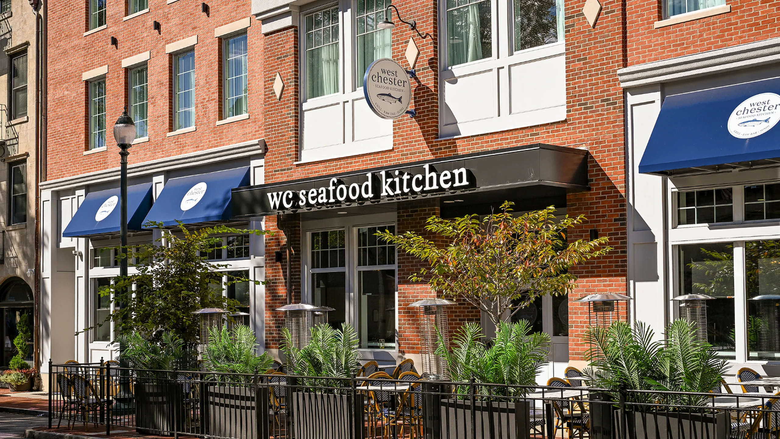 Charming brick facade of WC Seafood Kitchen adorned with stylish awnings and inviting outdoor seating, offering a vibrant dining experience.