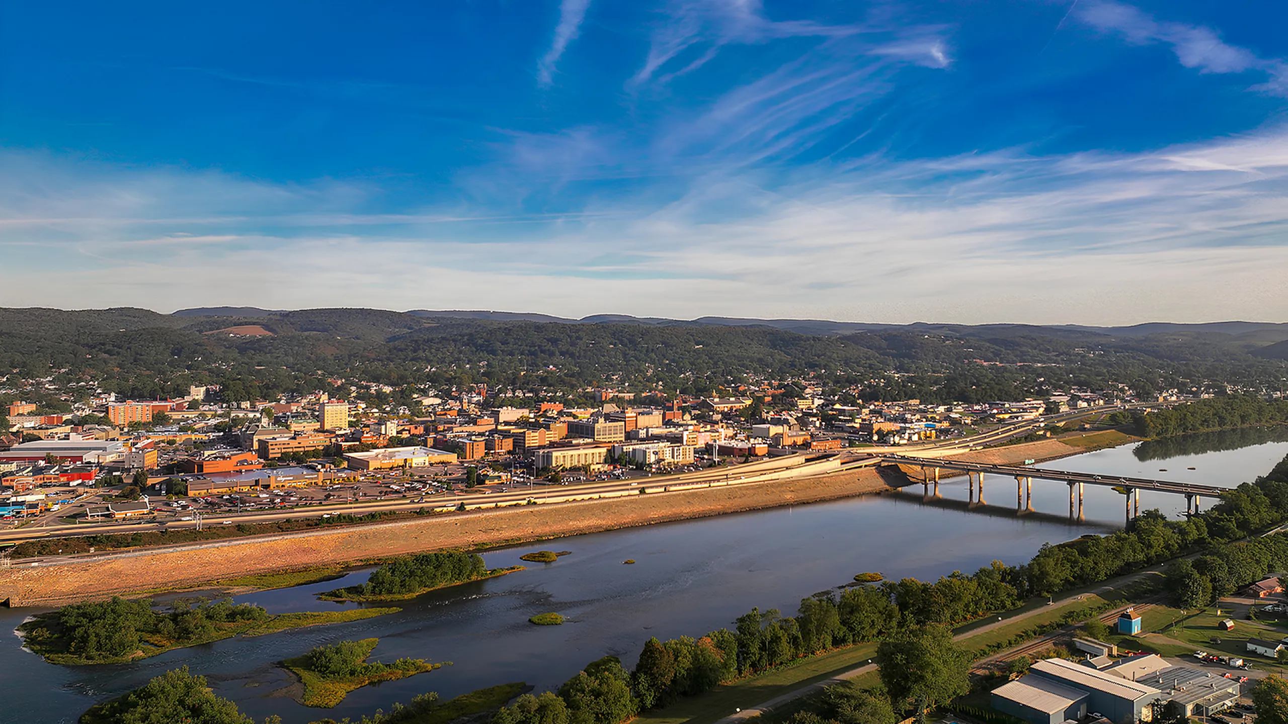 Stunning aerial view of a vibrant cityscape with a flowing river and lush green hills under a clear blue sky.