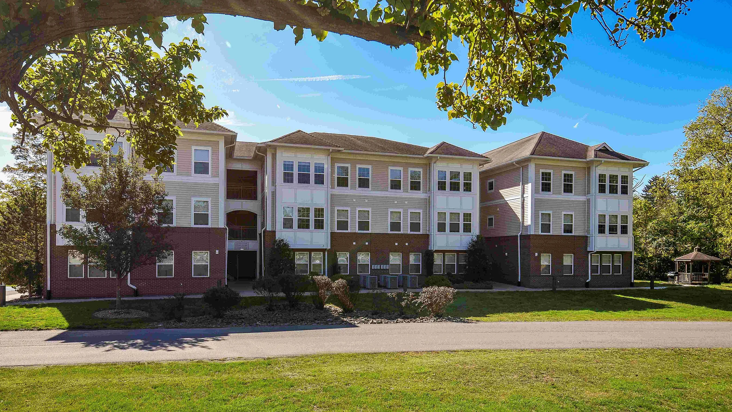 Charming multi-story apartment building with elegant brick and siding facade, nestled in a lush, green landscape under a vibrant blue sky.