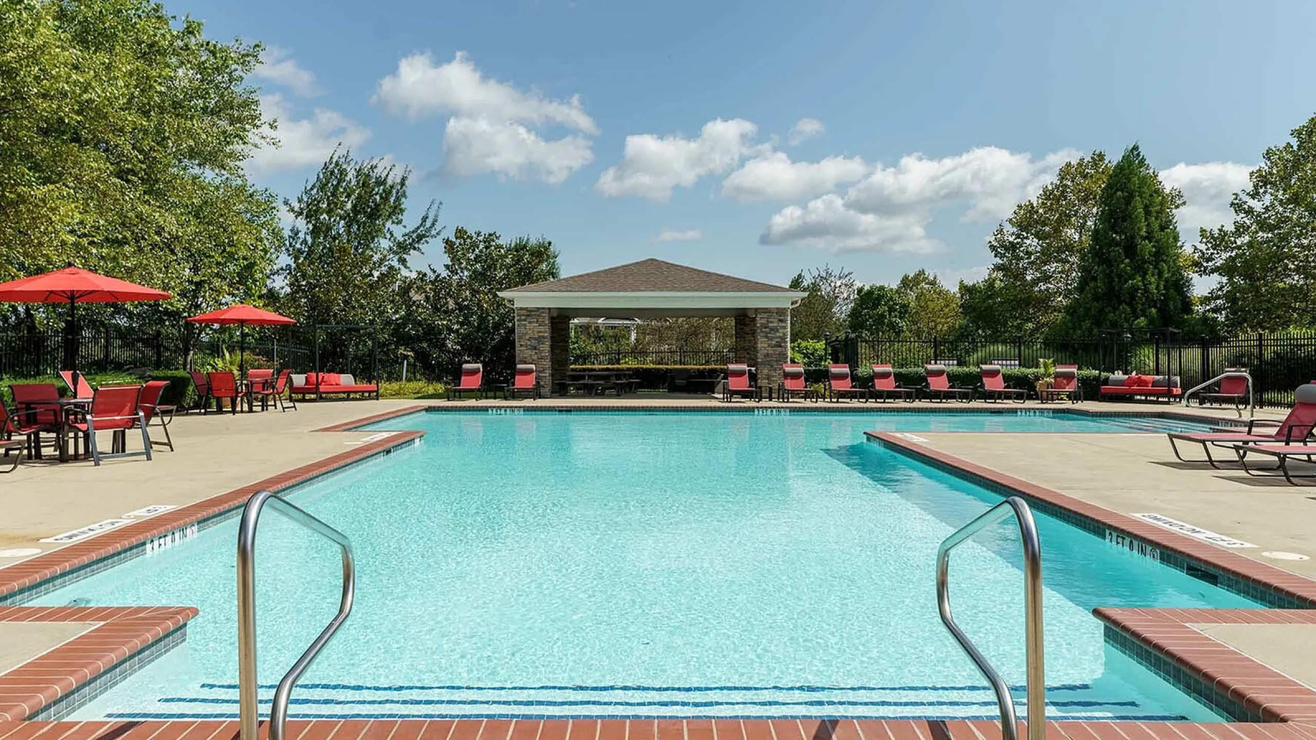 Inviting outdoor pool with clear blue water, surrounded by red lounge chairs and umbrellas, ideal for relaxation and sunbathing.