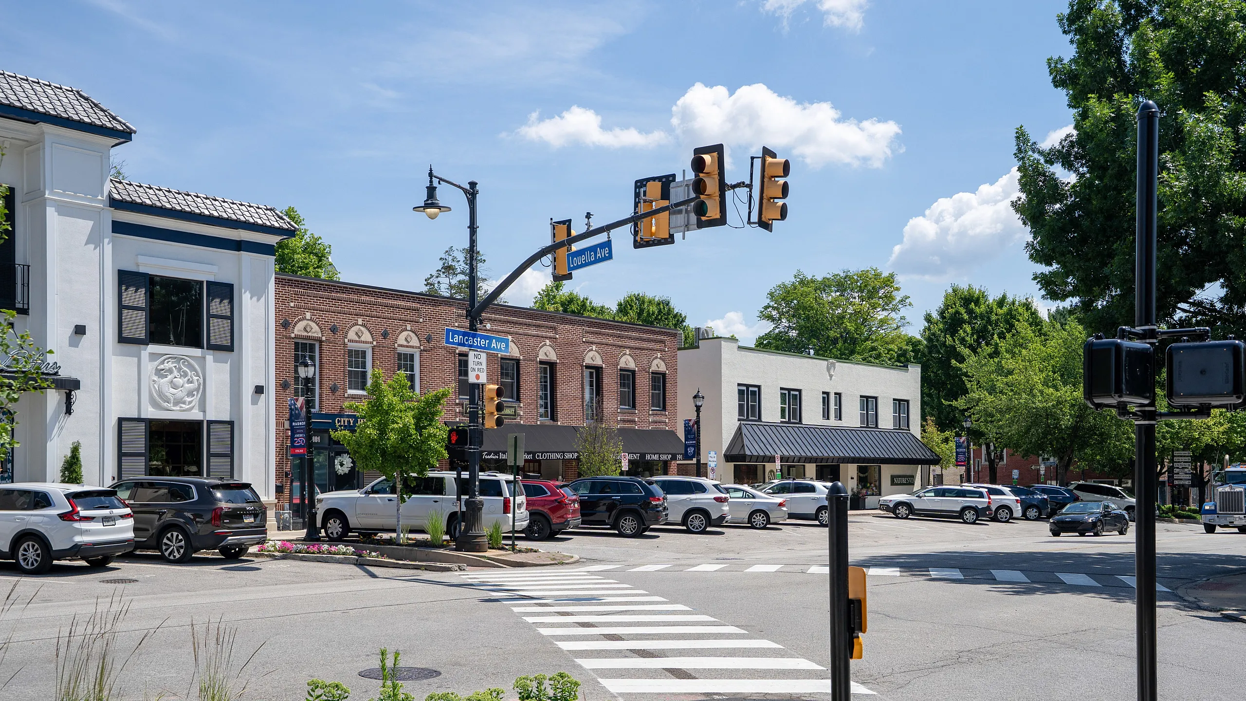 Charming downtown intersection with vibrant shops, lush trees, and a clear blue sky, perfect for urban living.