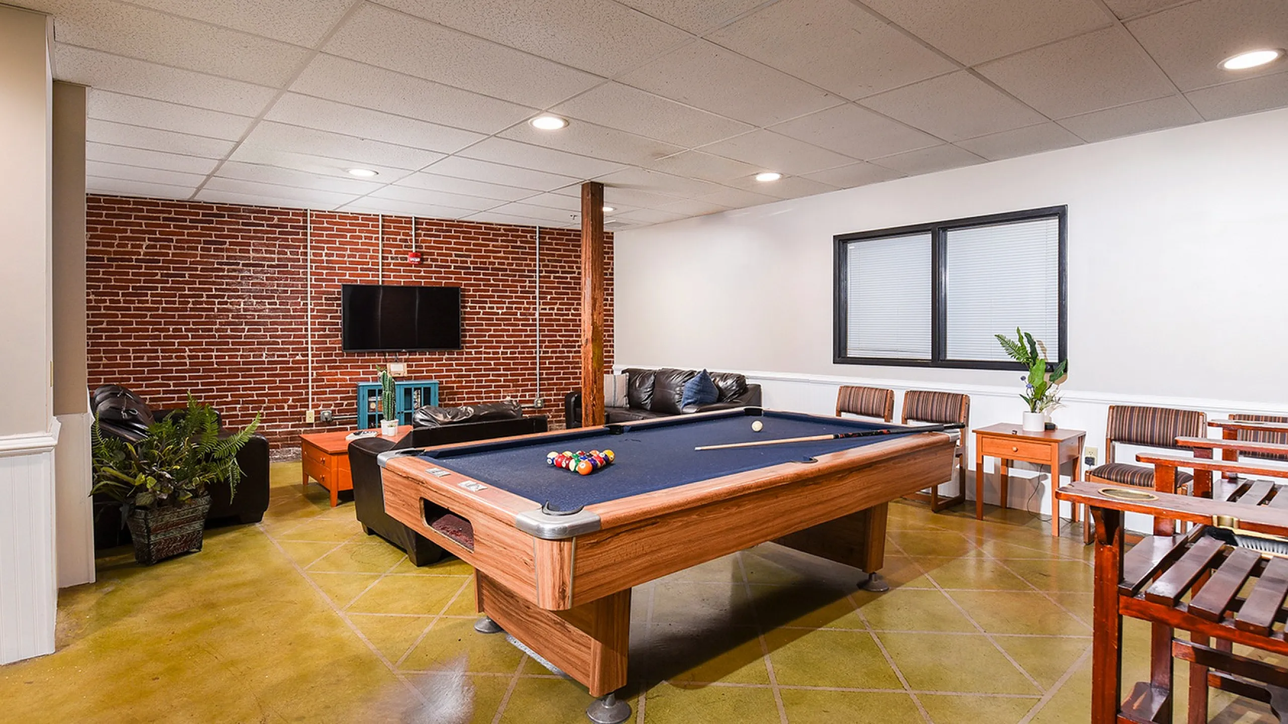 Inviting game room with a modern pool table, cozy seating, and stylish brick accent wall for ultimate relaxation.