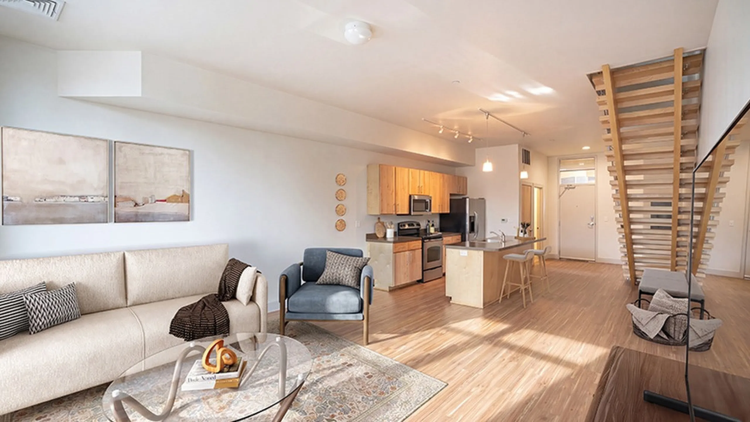 Modern open-concept living room and kitchen with stylish furniture, elegant decor, and wooden staircase in a bright, spacious apartment.