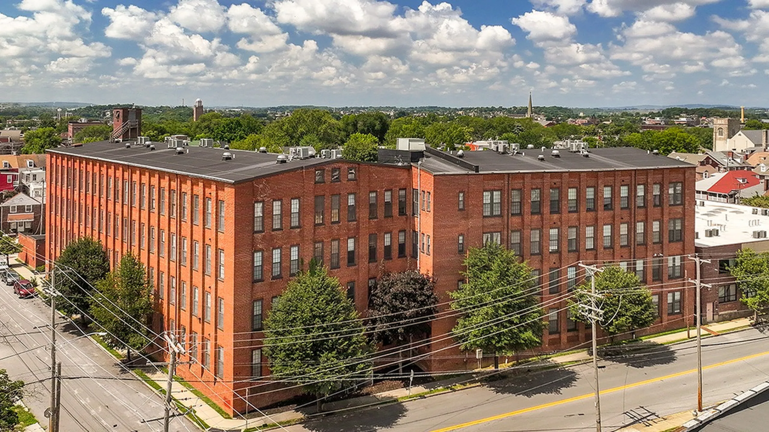 Impressive aerial view of a historic brick apartment building with large windows, surrounded by lush greenery in a vibrant urban neighborhood.