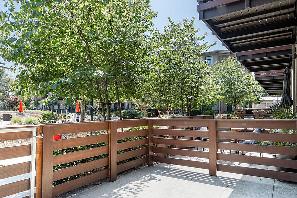 Inviting apartment patio with wooden railing, lush trees, and a view of a vibrant courtyard.
