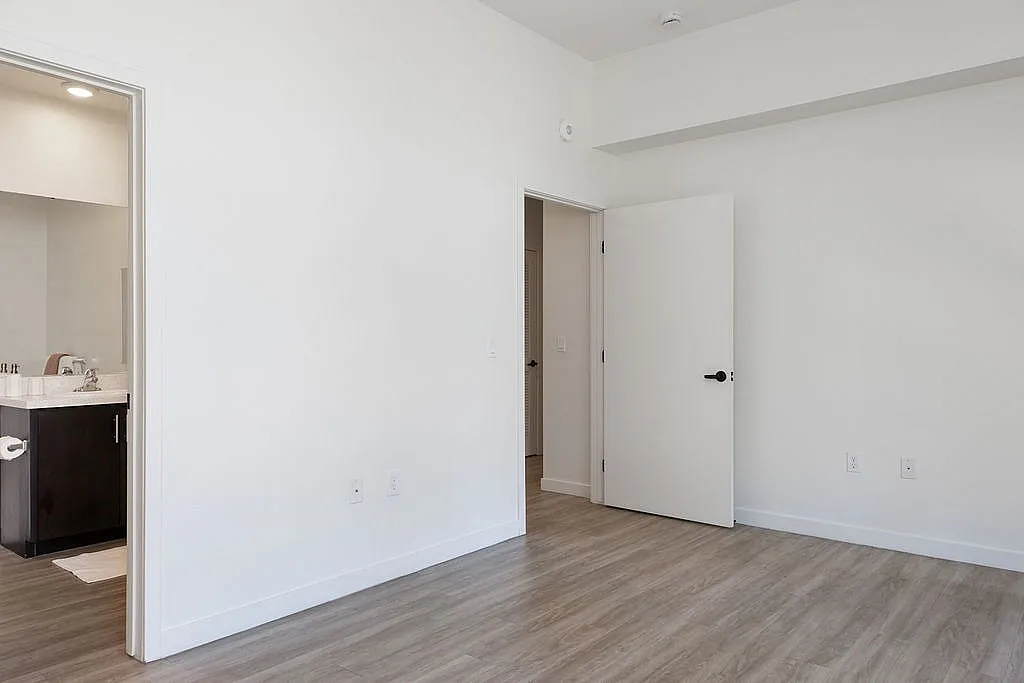 Bright and airy bedroom featuring sleek hardwood flooring, contemporary bathroom access, and modern finishes.