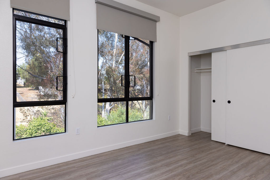Bright and airy bedroom with large windows, modern flooring, and ample closet space, offering serene outdoor views.