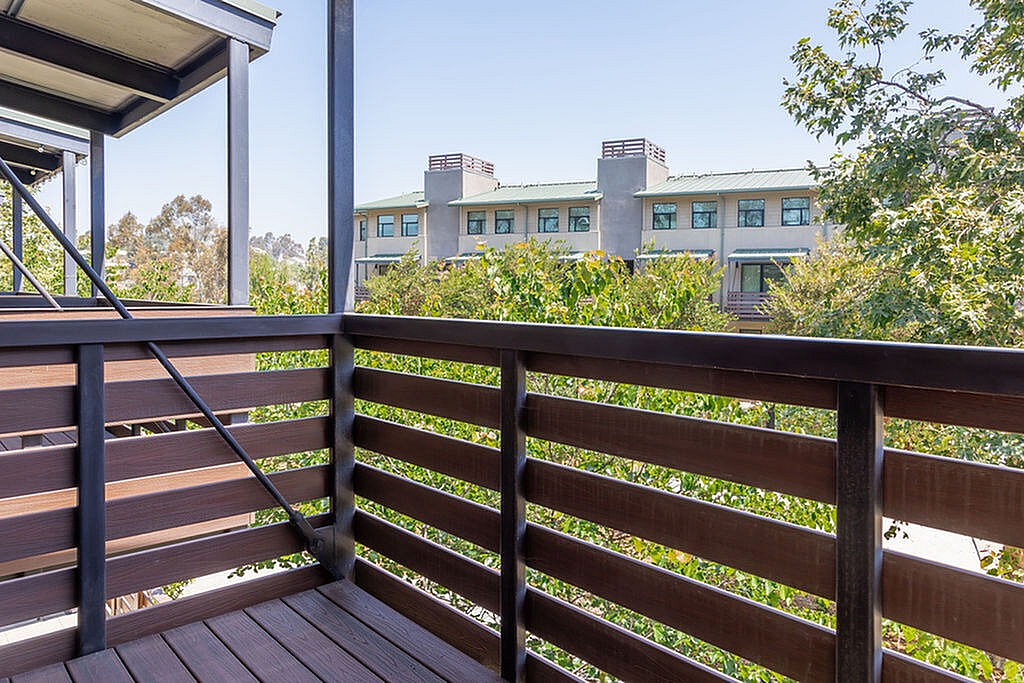 Charming balcony view with lush greenery and modern apartment buildings under a clear blue sky.