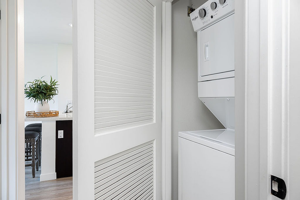 Convenient in-unit laundry with modern stackable washer and dryer, complemented by sleek interior design and inviting kitchen view.